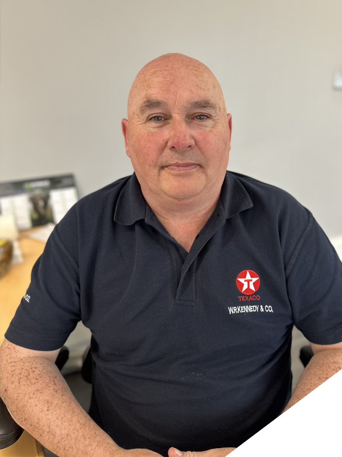 A bald man wearing a navy polo shirt with a Texaco logo sitting at a desk in an office.