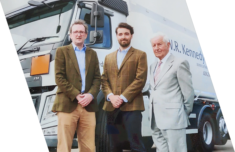 Three men in business attire standing in front of a large truck.