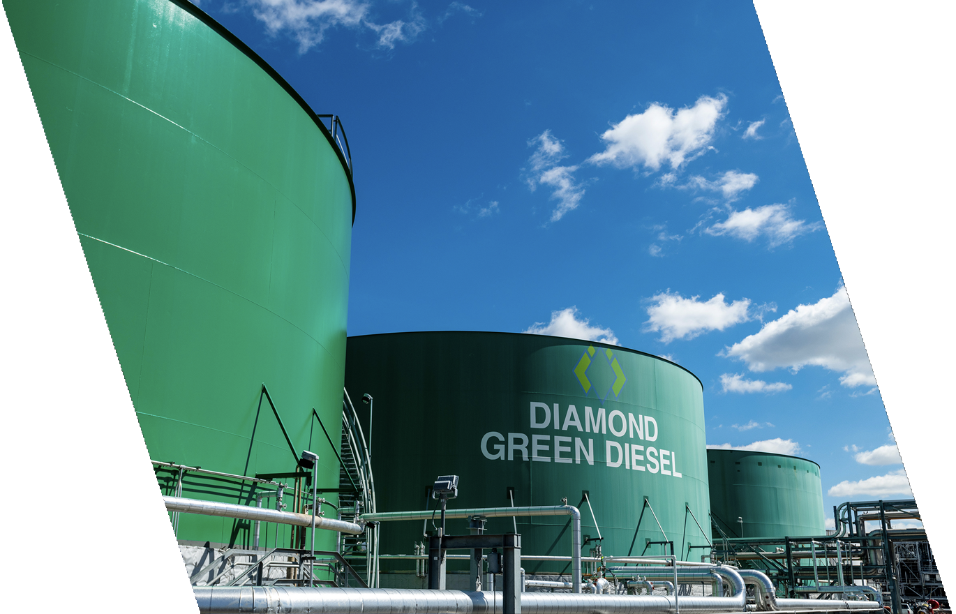 Industrial tanks labeled "Diamond Green Diesel" in a bright outdoor setting with a blue sky and clouds.