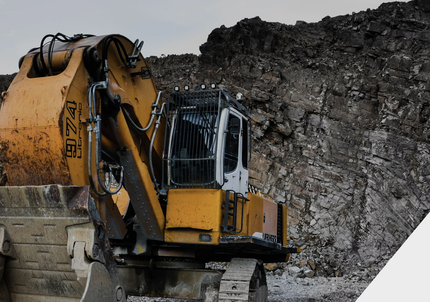 A yellow and white excavator working against a rocky cliff in a quarry or construction site.