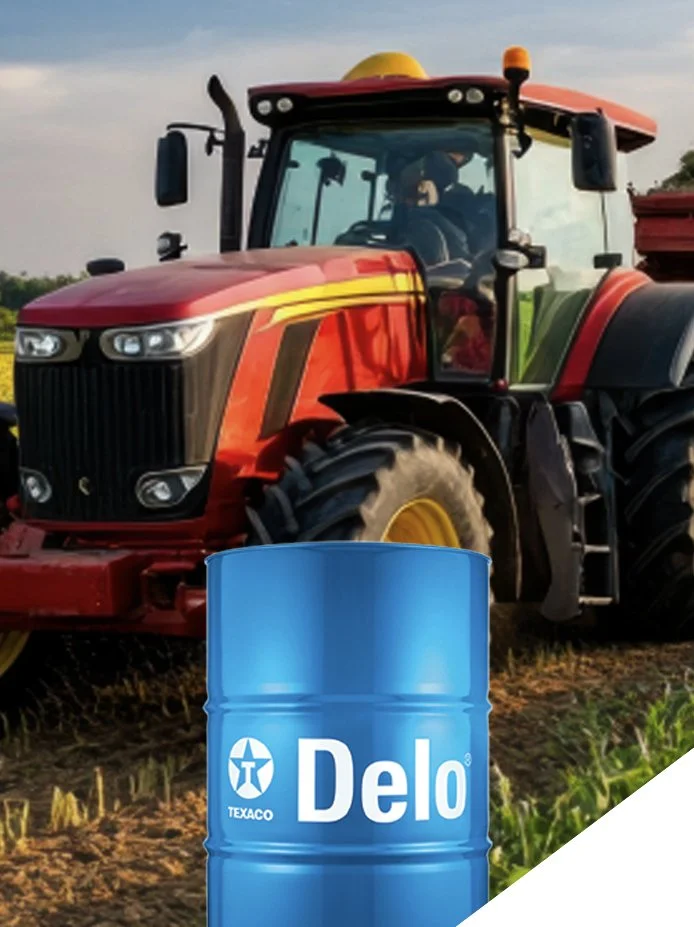 A red tractor is on a farm field with a blue Delo oil barrel in the foreground.
