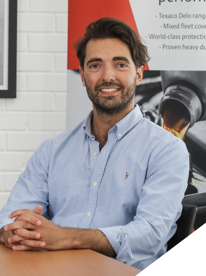 A man sitting at a table in front of a white brick wall and a poster about performance oils.