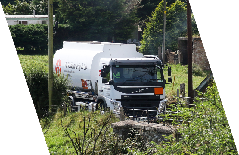 A white tanker truck with the logo 'M.R. Kennedy & Co' parked along a rural road surrounded by greenery and trees.