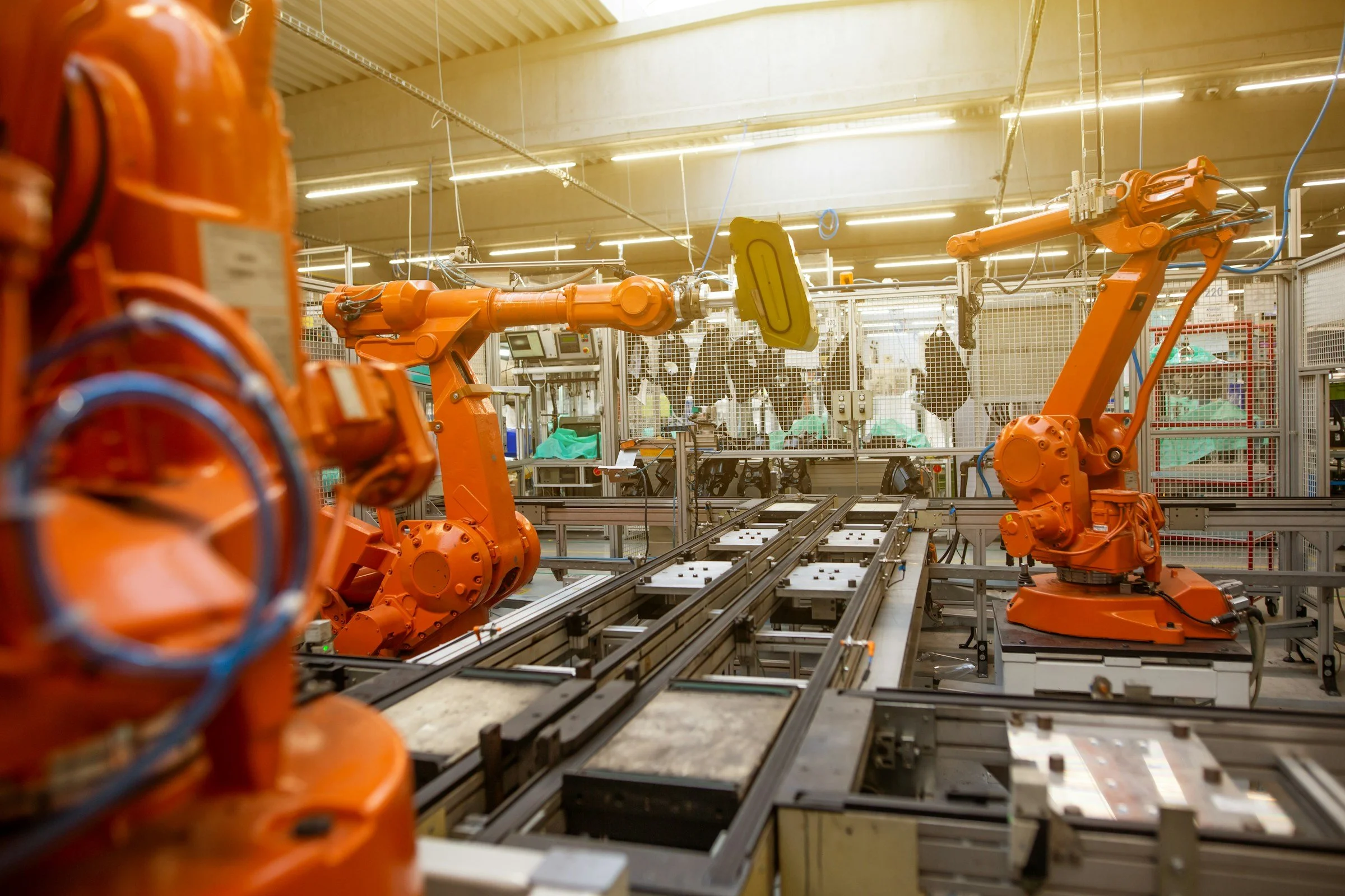 Industrial factory with orange robotic arms working on assembly line, surrounded by machinery and safety fencing.