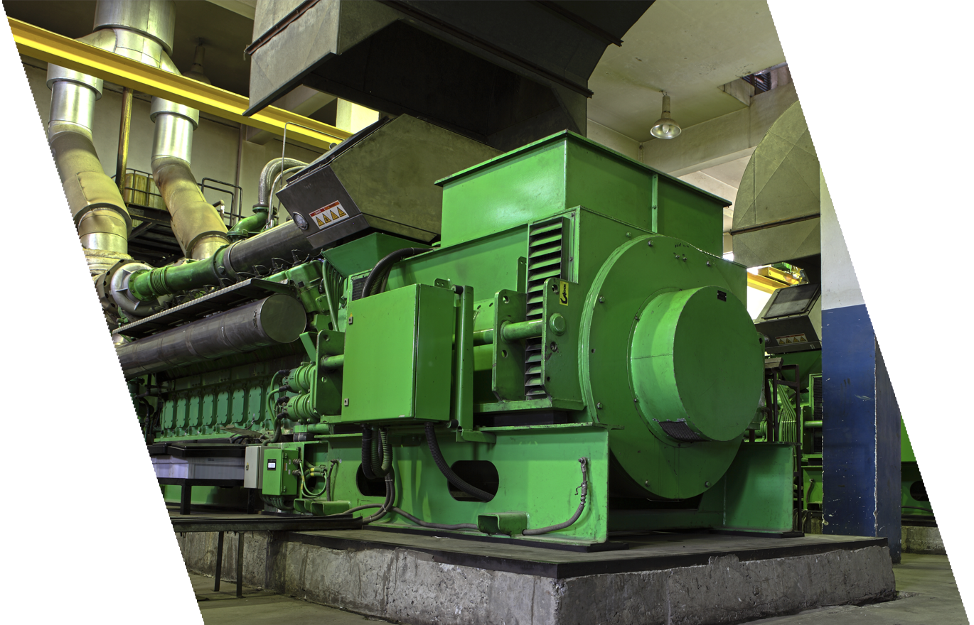A large green industrial machine in a factory setting, with pipes and ventilation ducts around it.
