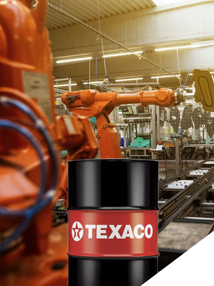 Industrial manufacturing facility with a robotic arm and a Texaco oil barrel in the foreground.