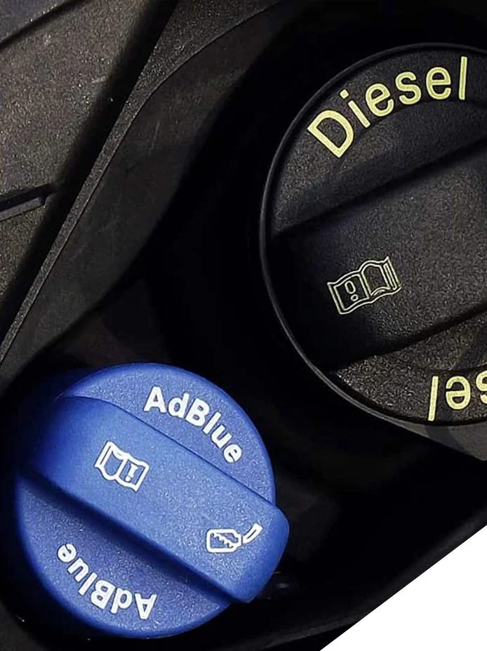 Close-up of a vehicle dashboard showing a blue AdBlue cap with symbols for windshield washer fluid and engine oil, and a black diesel fuel cap with a symbol of a fuel pump and the word "Diesel".