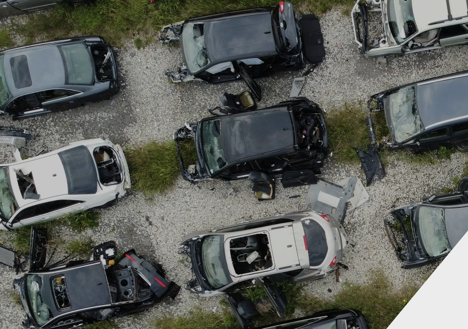 Aerial view of a salvage yard with damaged cars, some missing parts, and debris on gravel ground.