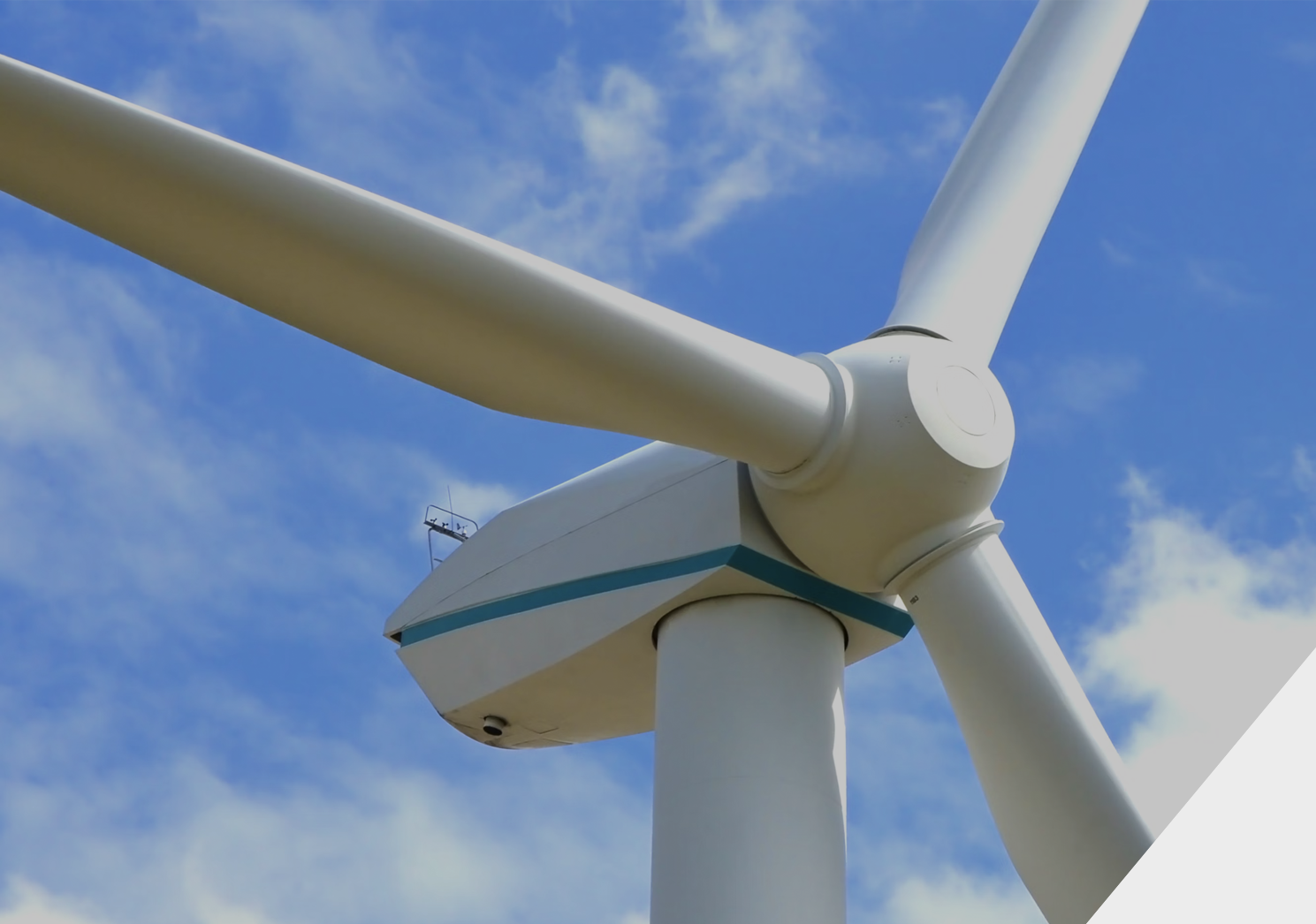 Close-up of a large white wind turbine against a blue sky with clouds.
