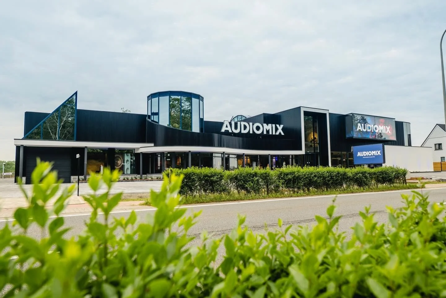 Modern zwart en witte audiomix winkel met grote schermen en glasdetails, omgeven door groen en een weg voor de winkel.