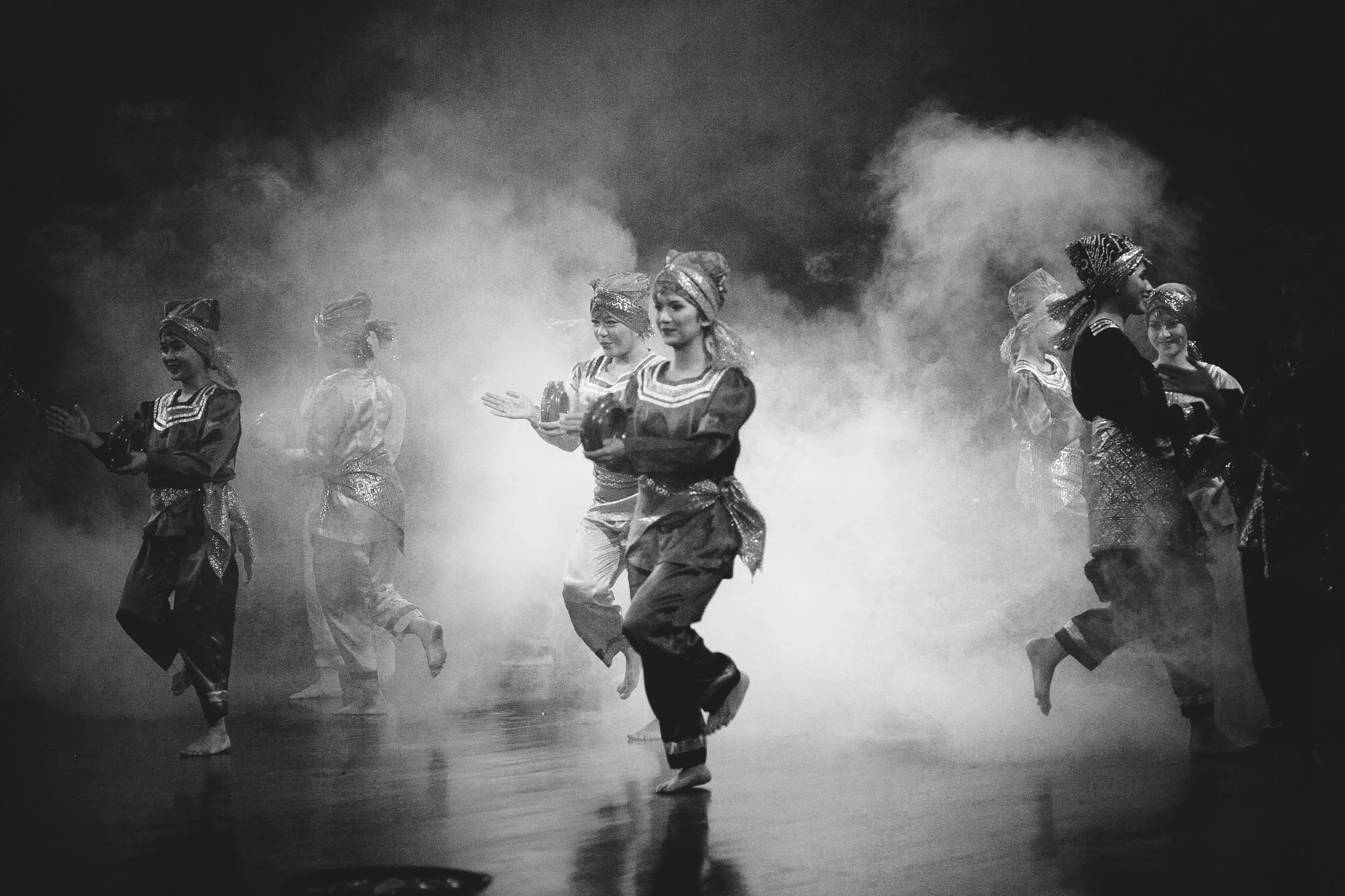 A group of dancers in traditional costumes performing on stage with smoke effects.