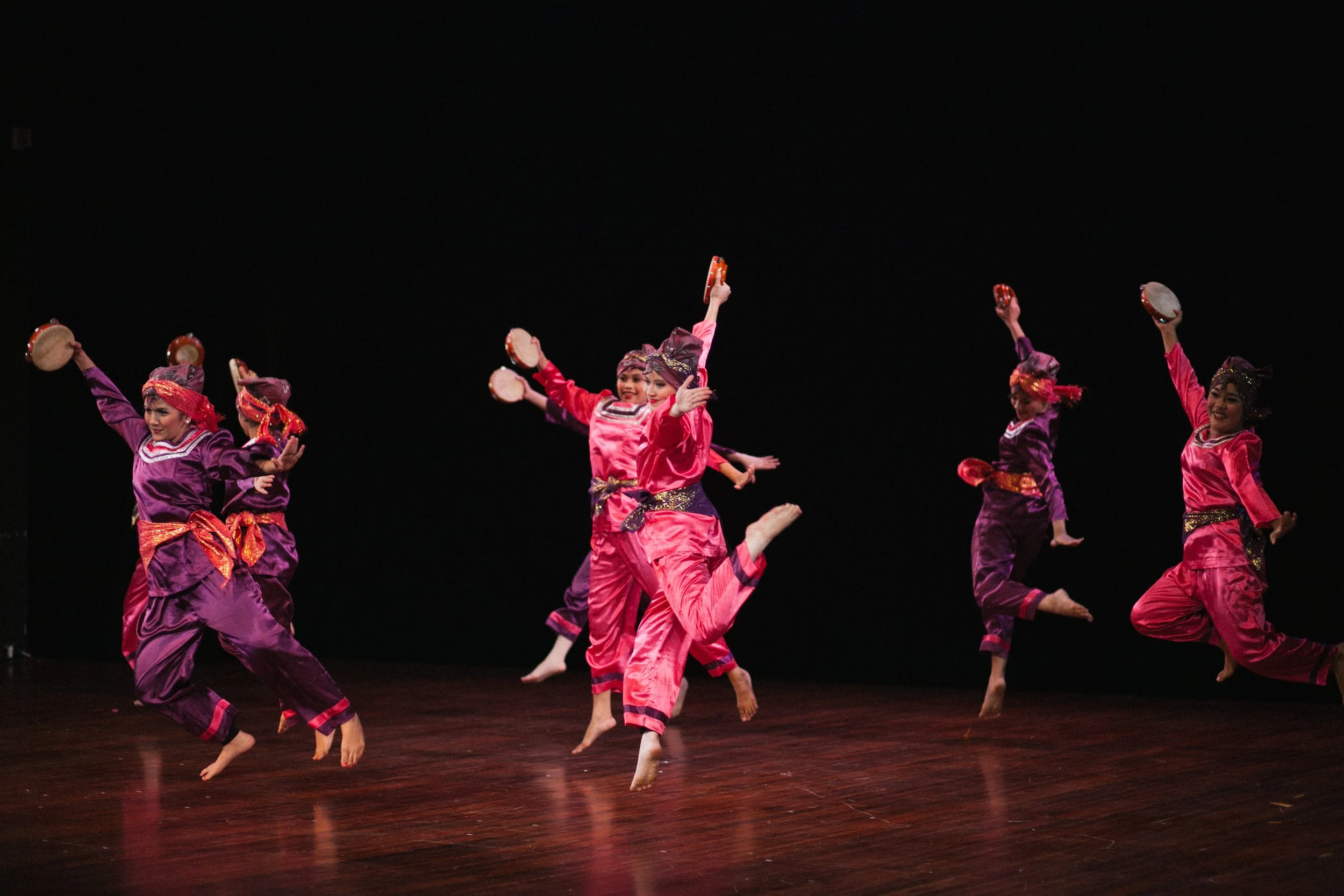 Group of dancers in traditional Asian costumes performing on stage with tambourines.