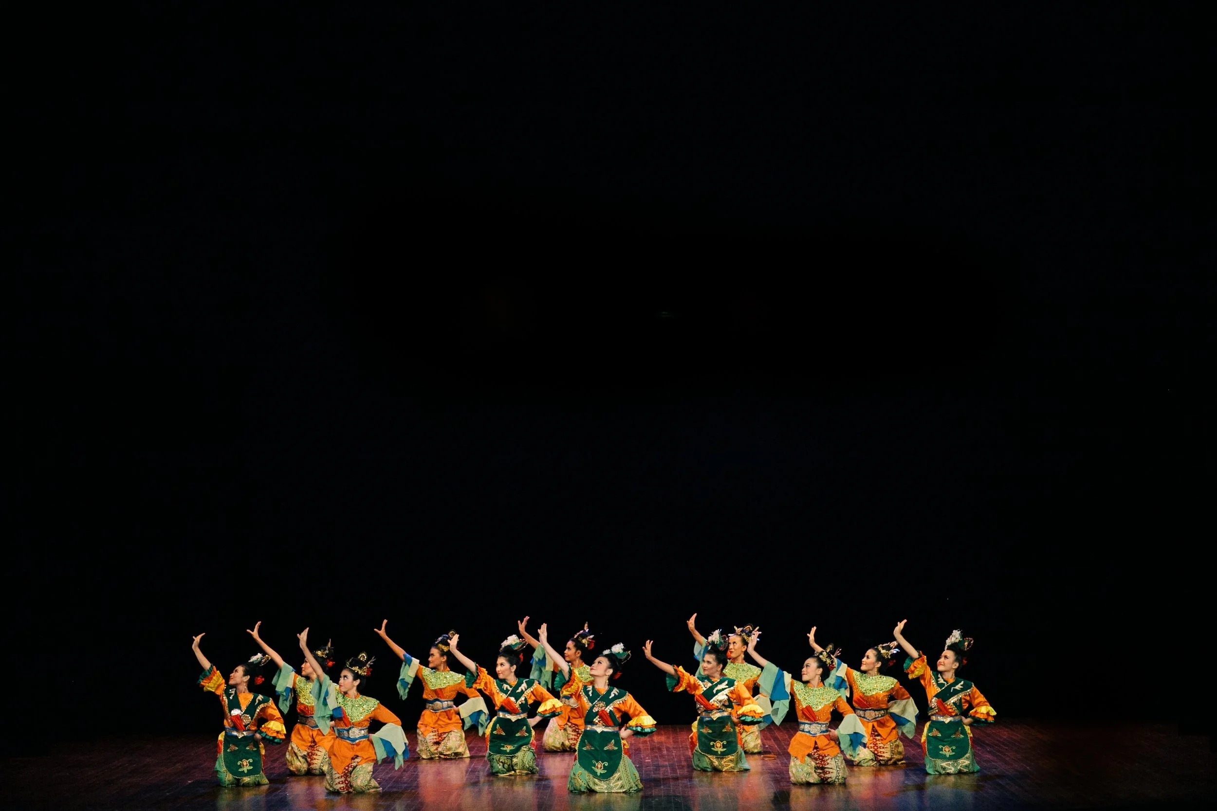 Group of dancers in colorful traditional costumes performing on stage against a black background.