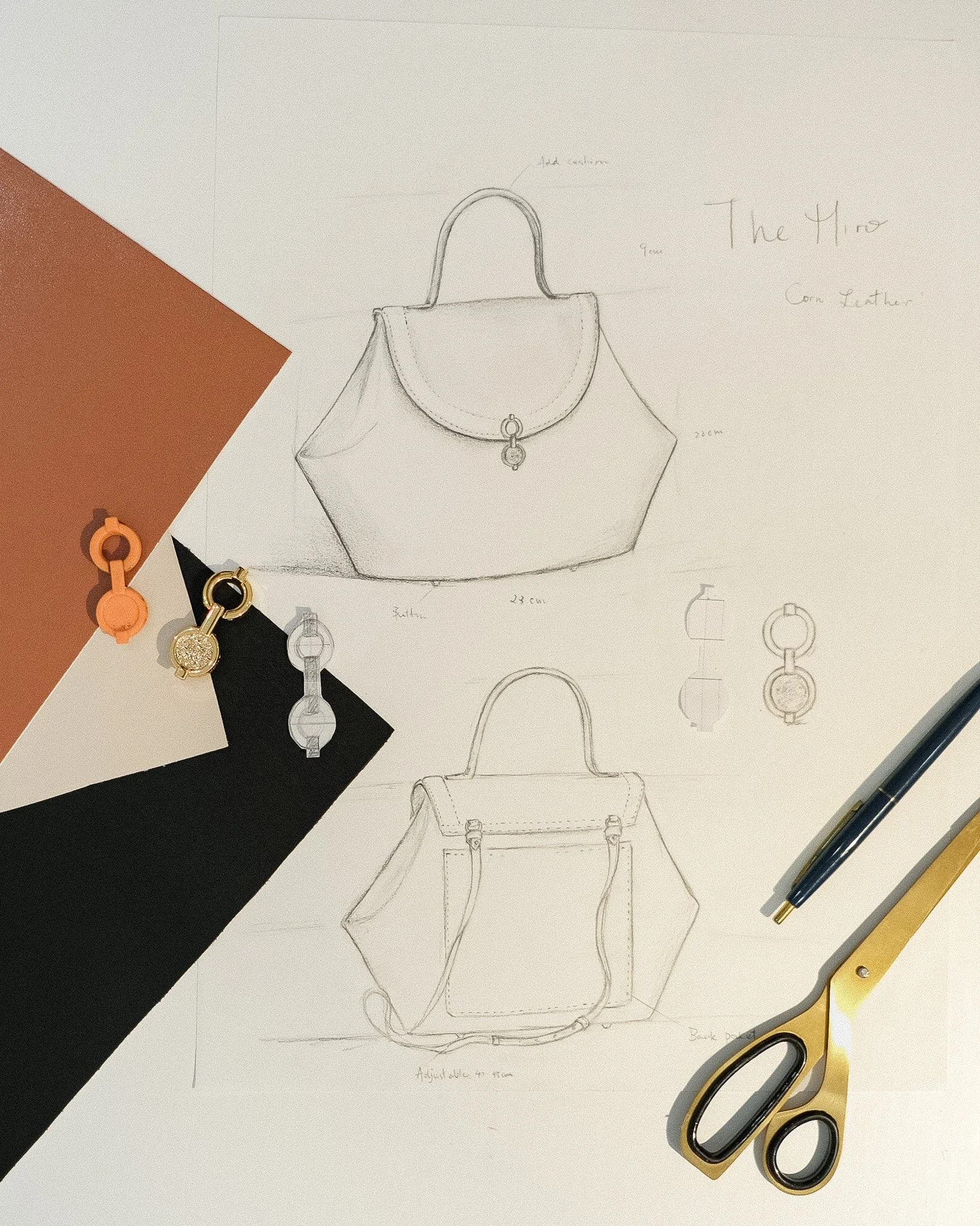 Sketch of a handbag design on paper, surrounded by color Swatches, with a pair of black and white glasses, and black and yellow pens.