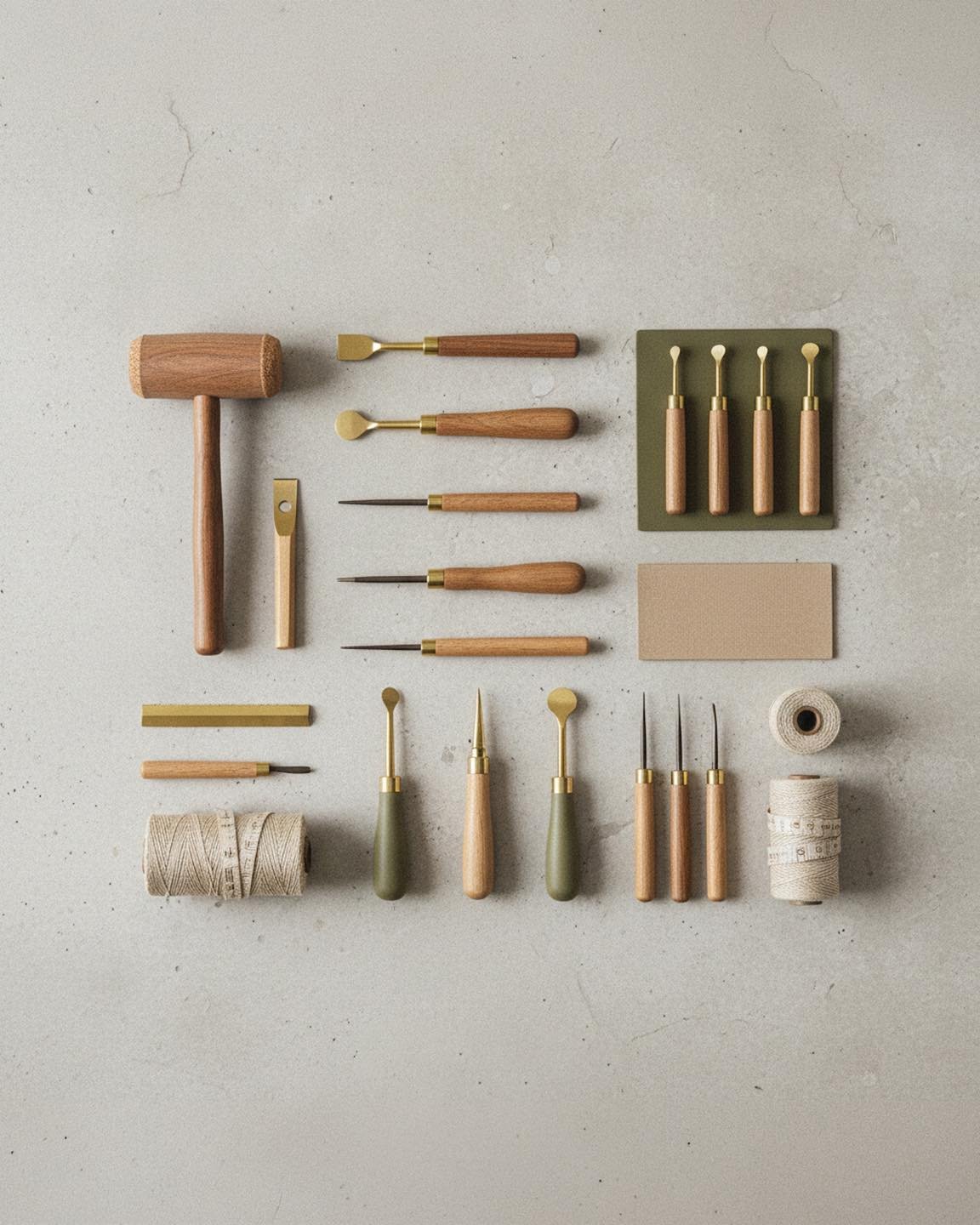 Various woodworking tools, including hammers, chisels, gouges, and carving knives, arranged on a light gray surface with some spools of string nearby.