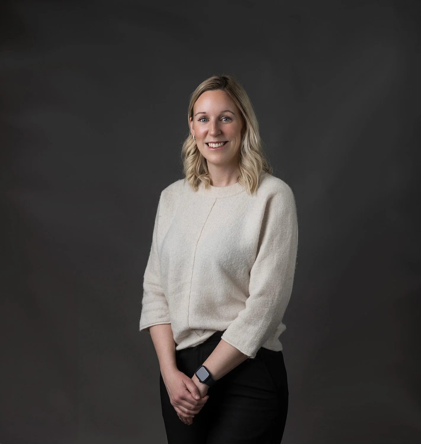 Sexualrådgivare Johanna Löfberg med blont hår, beige tröja och svarta byxor står mot en svart bakgrund.