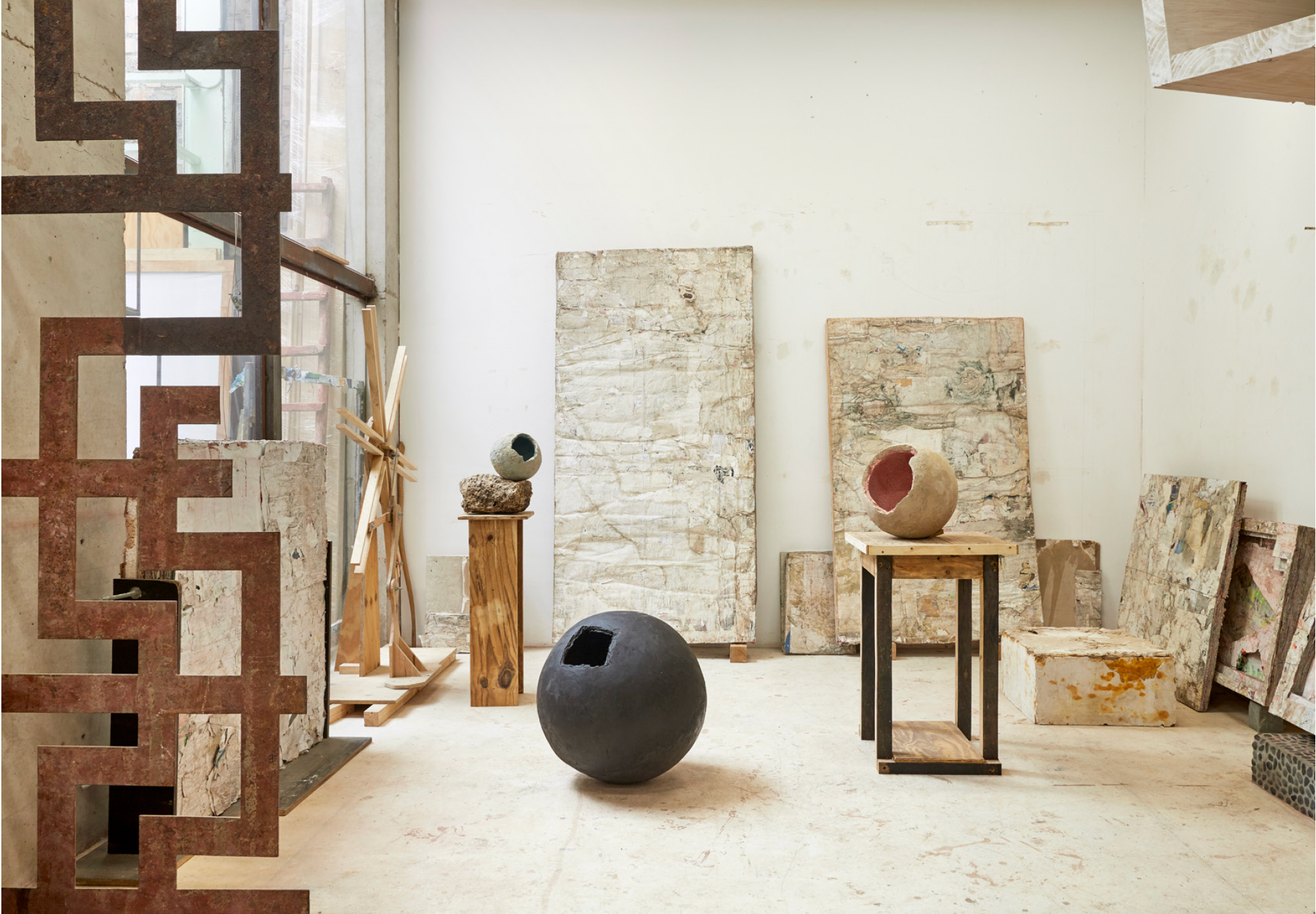 Art studio with sculptures and canvases, featuring a large black spherical sculpture, a round sculpture with a hole, and various canvases leaning against the wall.