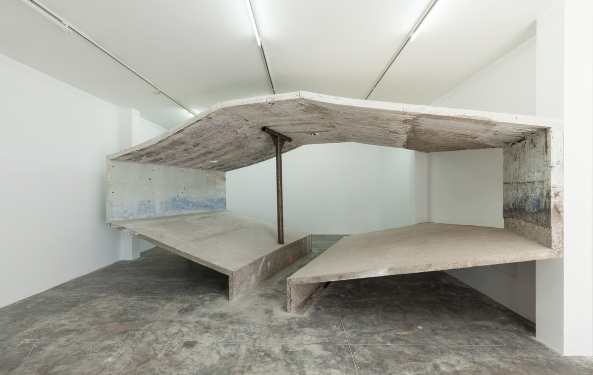 Gallery with large installation by Miguel Andrade Valdez that resembles an architetural structure spanning wall to wall  in the shape of the Petro Peru sign.