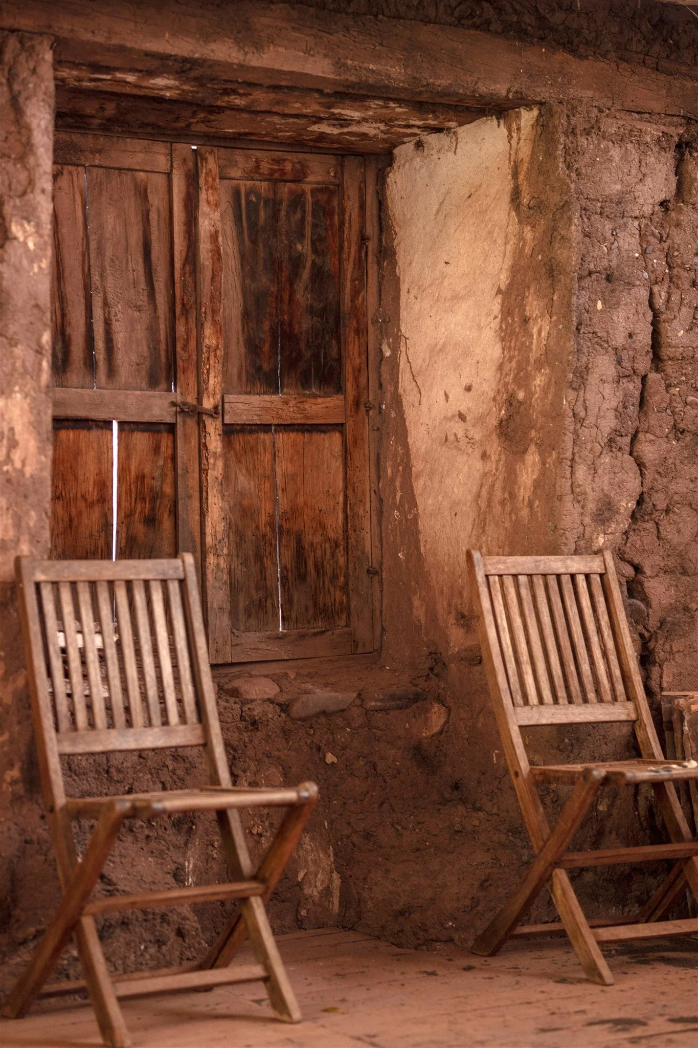 Interior of a rustic room with a wooden door, wooden chairs, and dirt walls.