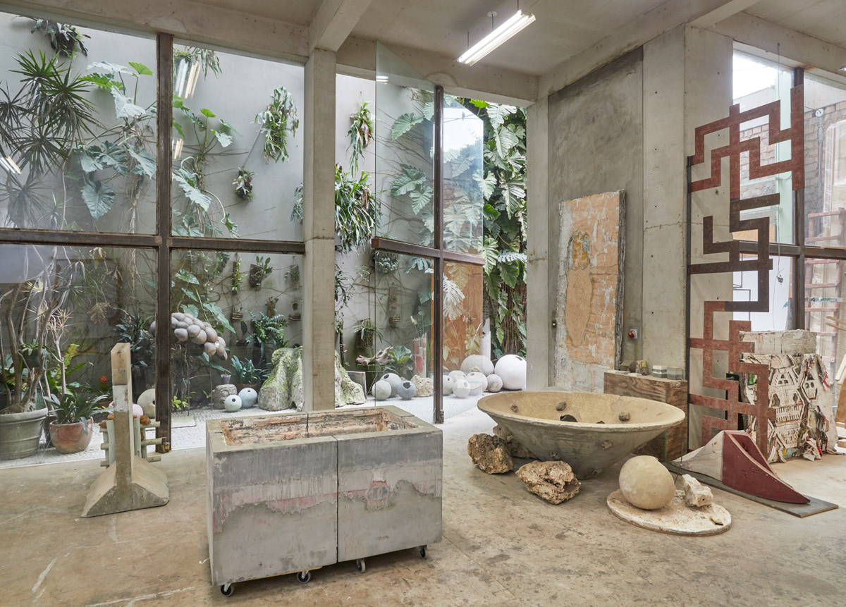 Artist's studio with large sculptures, paintings and a view of a courtyard with plants.
