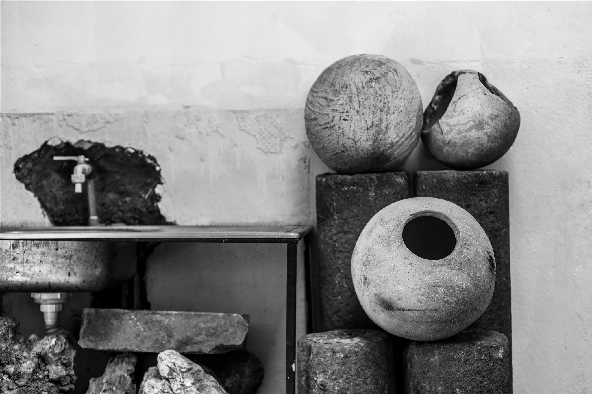 A black and white photo of three decorative vases or bowls stacked on top of brick blocks, with a wall in the background.
