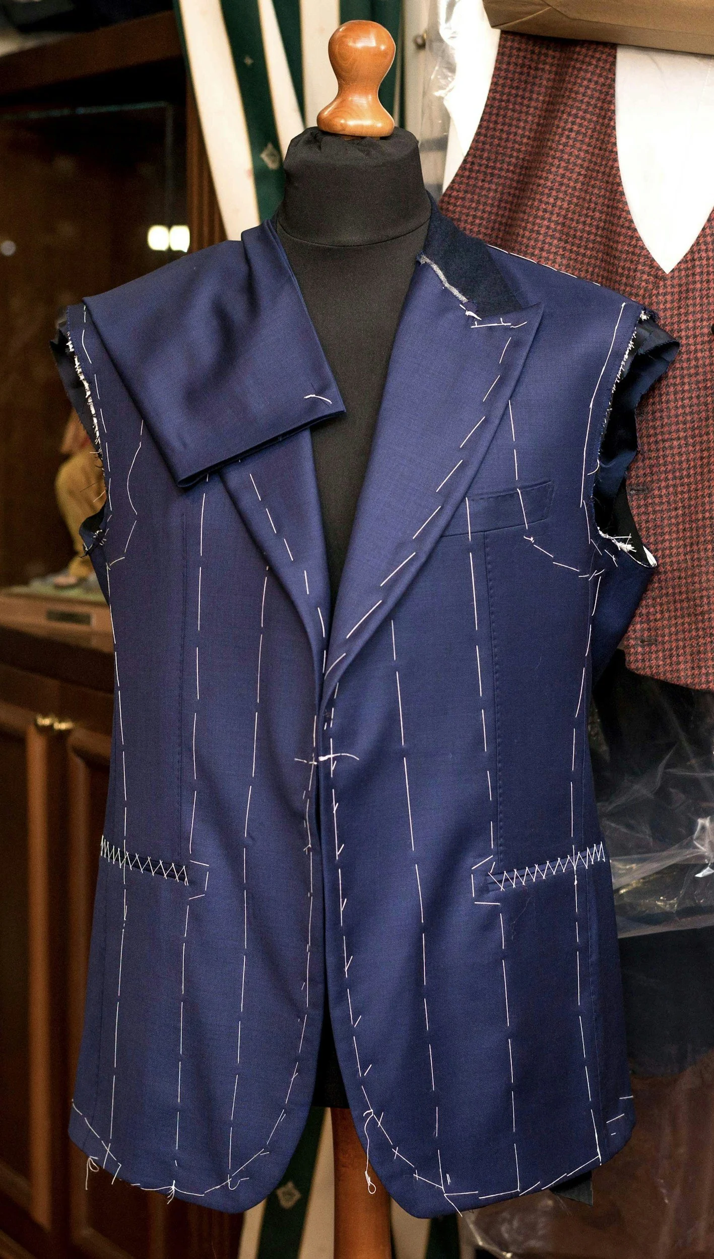 A tailors' bespoke suits with white chalk markings for tailoring, situated in a workshop. There is a piece of patterned fabric visible in the background.