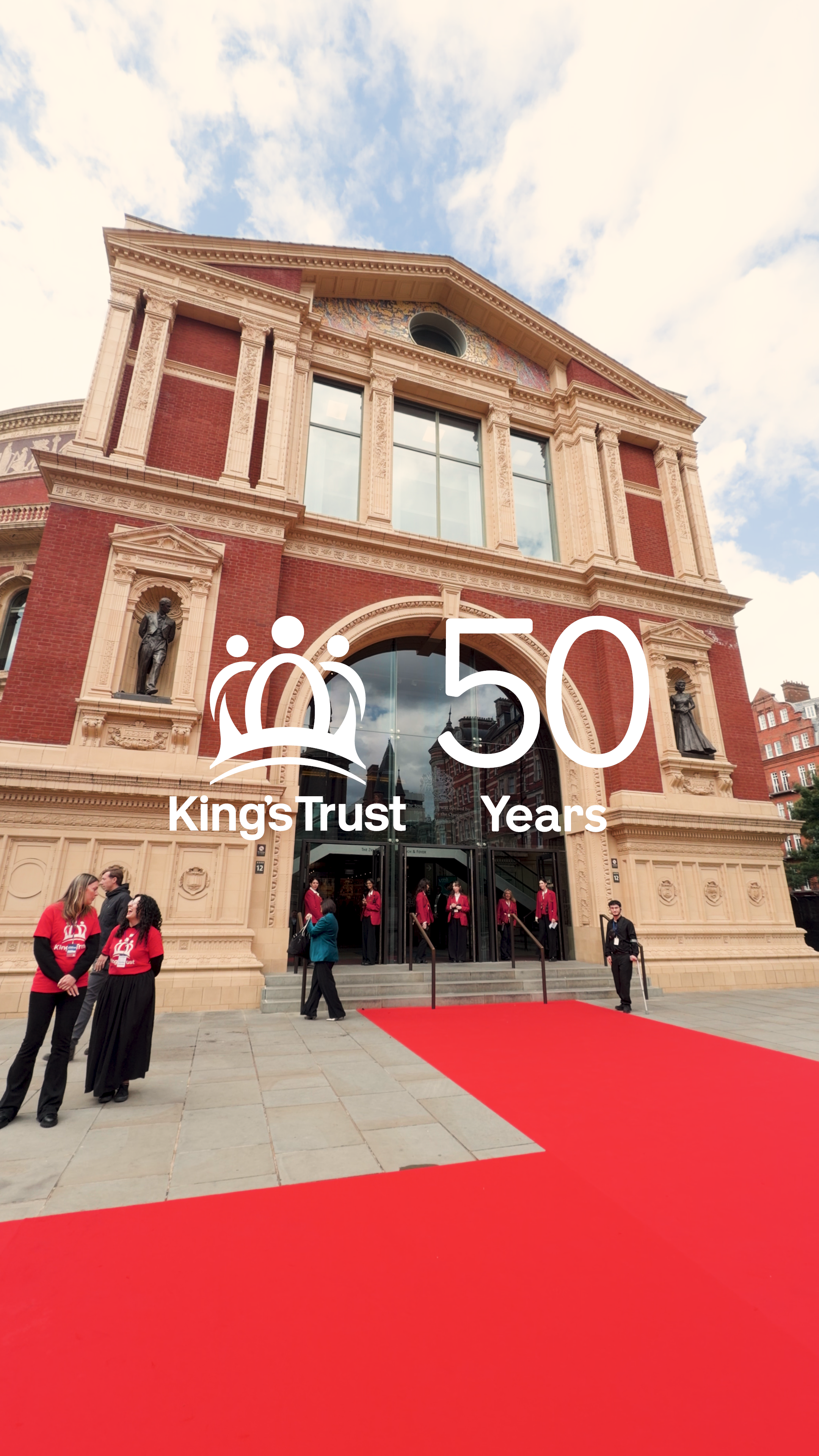 Celebrating 50 years of KingsTrust with a grand event at an elegant historic building with red brick facade, statues, large windows, and a red carpet with people in formal attire, some wearing red shirts with KingsTrust logo.