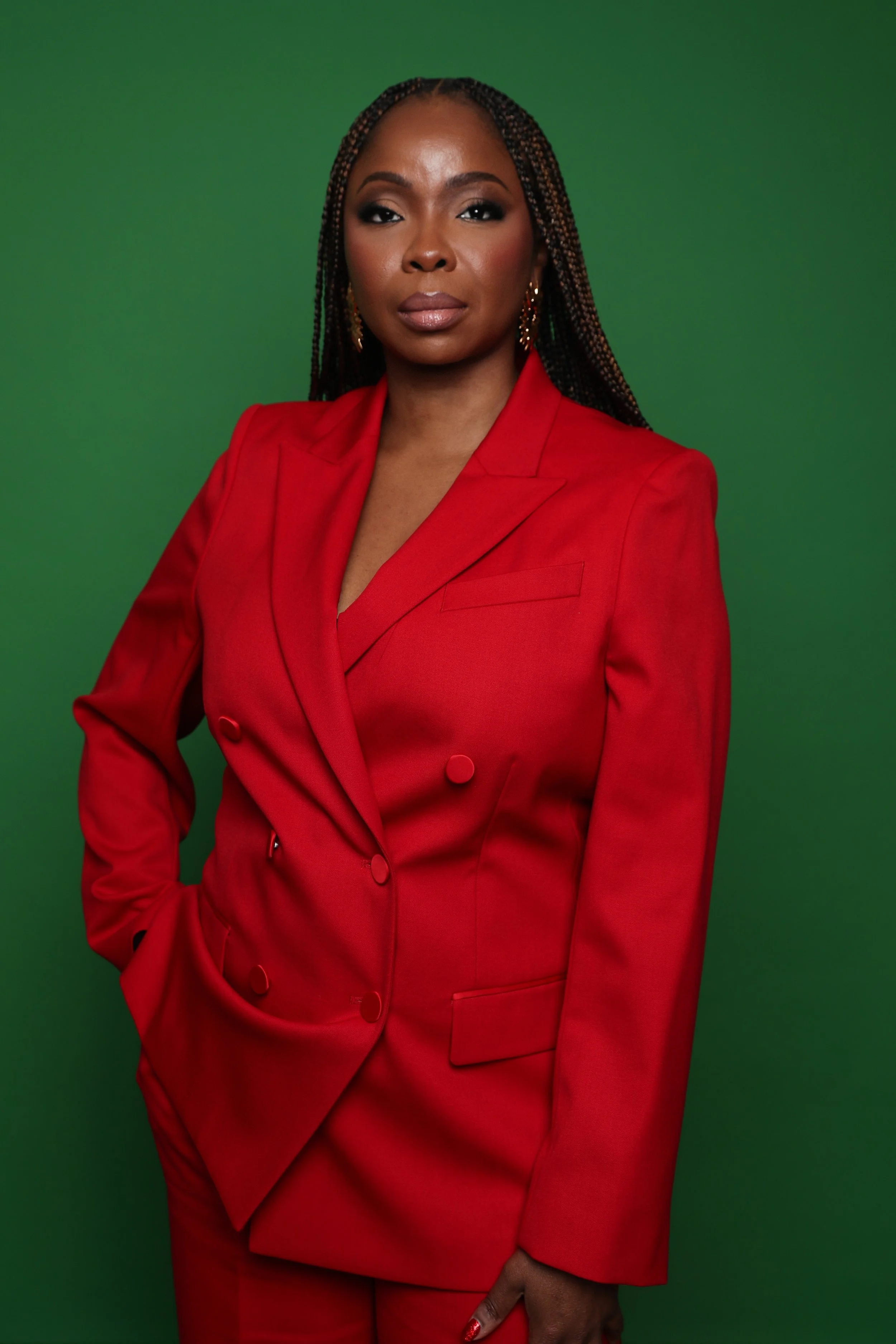 Eva Omaghomi wearing a red blazer against a green background.