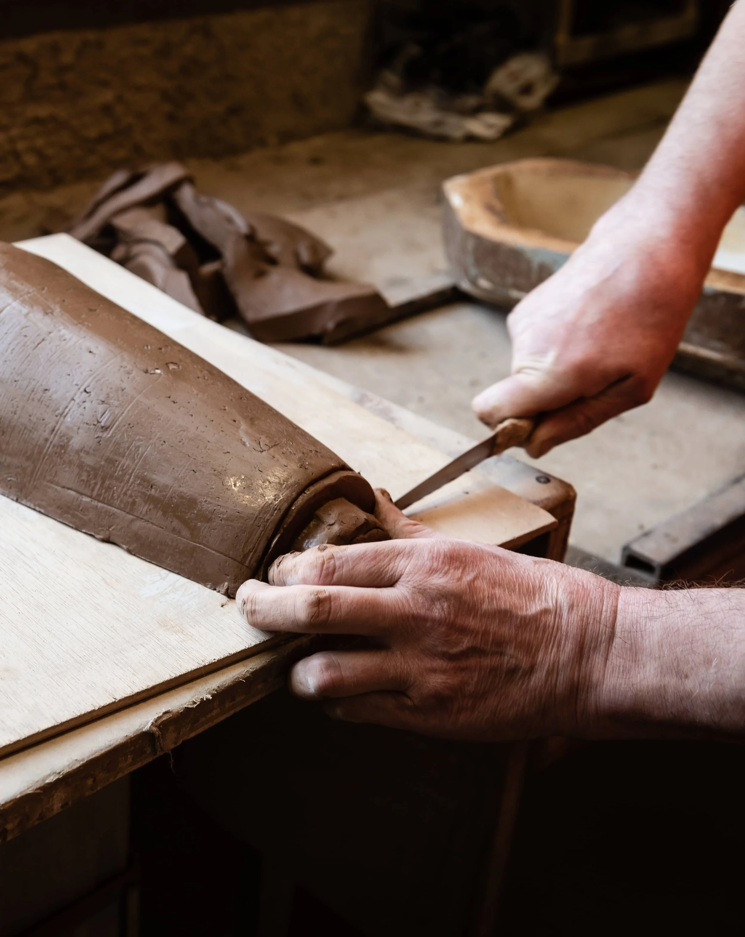 Main modelant une tuile, dans un atelier.
