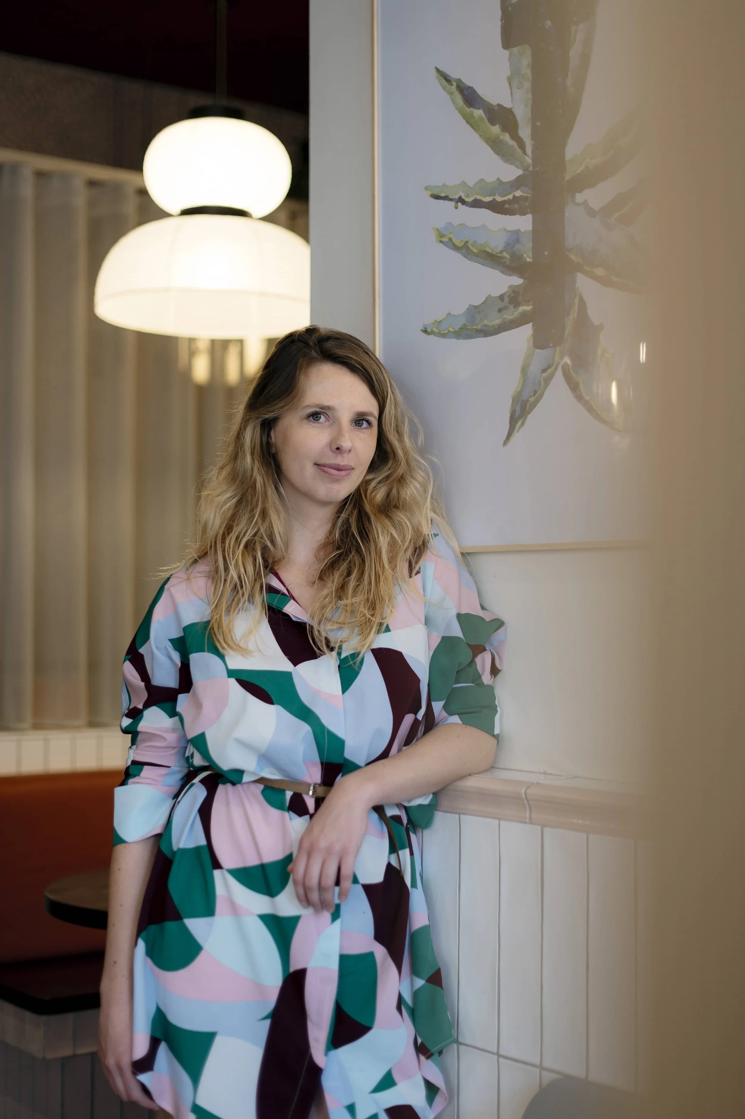 Portrait d'une femme aux cheveux longs, portant une robe colorée à motifs abstraits, à l'intérieur d'un lieu design.