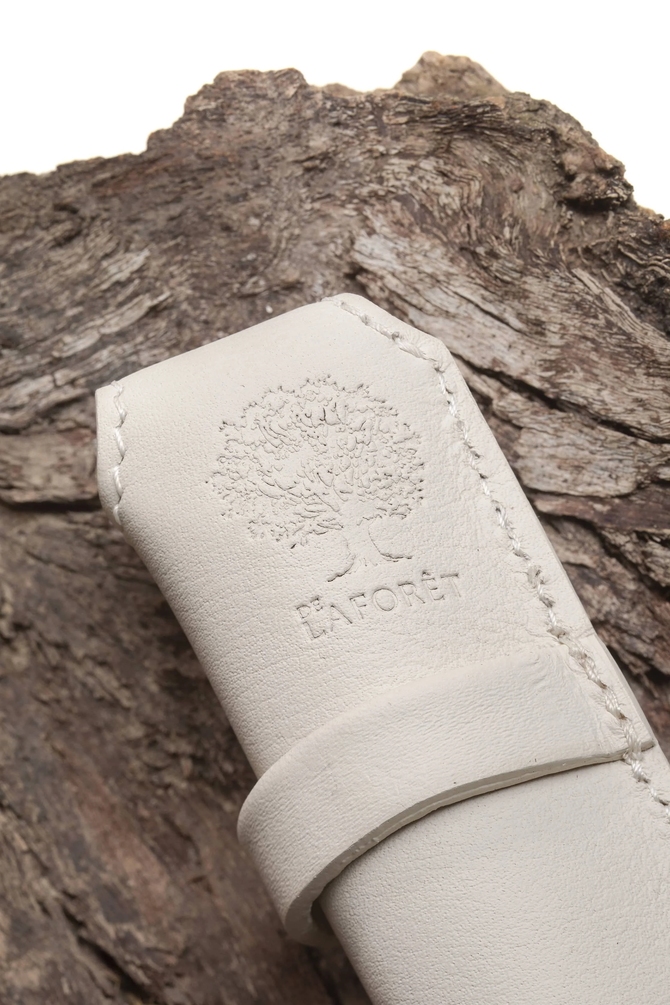 Un étui à stylo en cuir blanc avec le logo "De Laforet" gravé, posée sur une surface en bois.