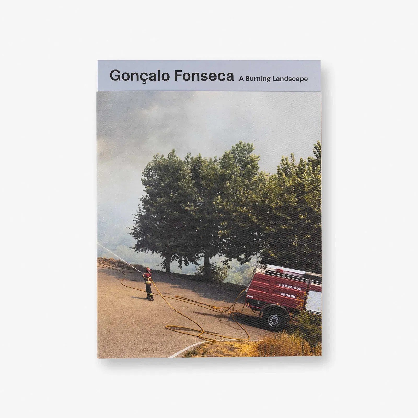Livro com capa mostrando uma cena de combate a incêndio com bombeiro usando mangueira de incêndio direcionada a uma árvore, e um caminhão de bombeiros ao lado, em um ambiente ao ar livre