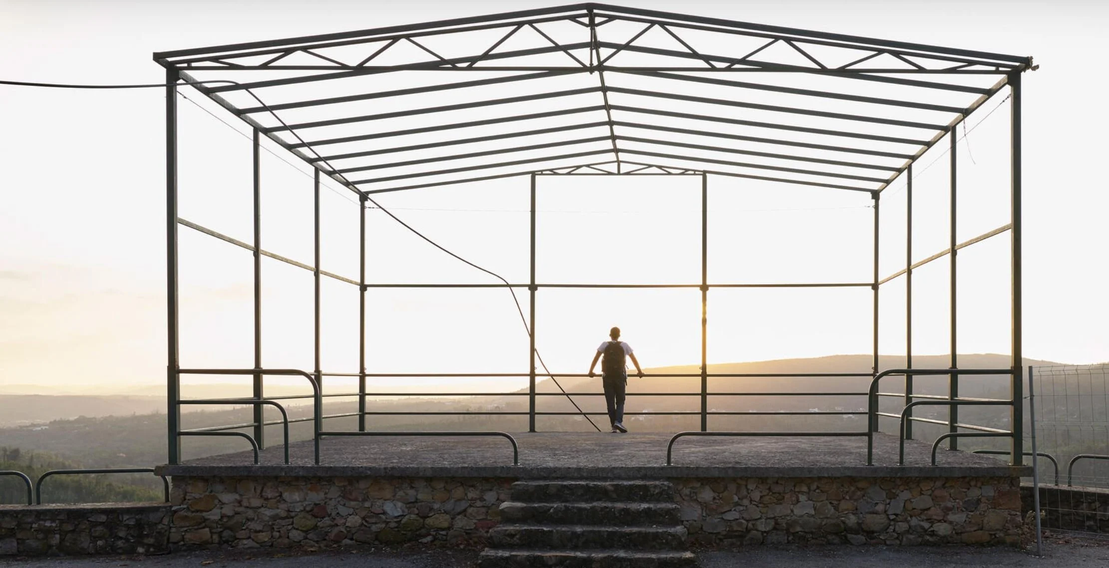 Pessoa caminhando em uma estrutura de palco ao ar livre ao pôr do sol