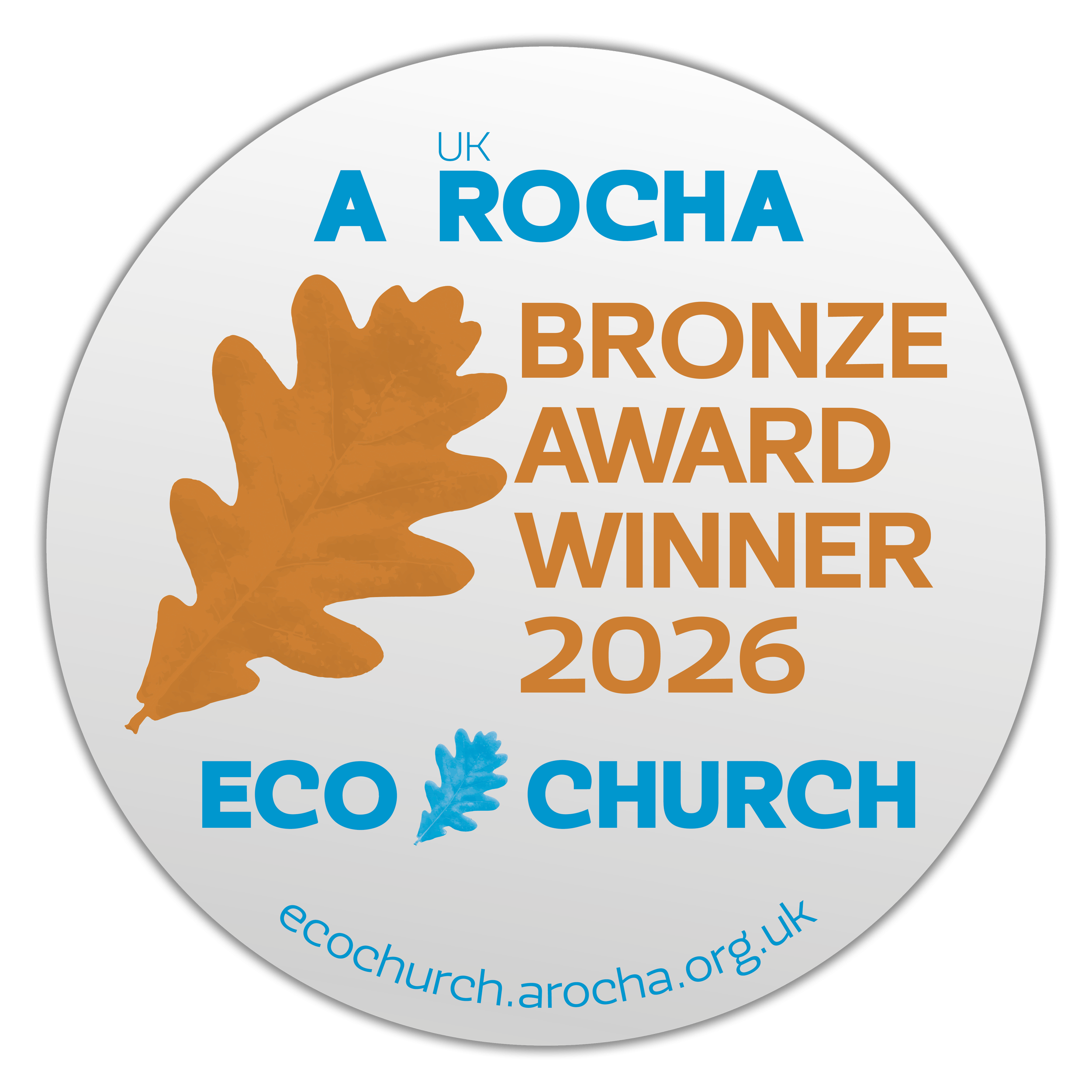 Circular badge with a white background and black border, featuring an orange oak leaf and a small blue oak leaf. The text reads: 'UK A ROCHA BRONZE AWARD WINNER 2026' in brown and blue, and at the bottom, 'eco@church.arocha.org.uk' in blue.