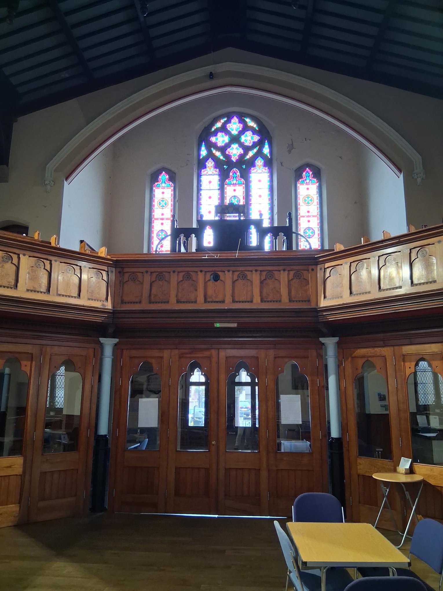 Interior view of a church or chapel with wooden paneling, stained glass windows, and high ceiling.