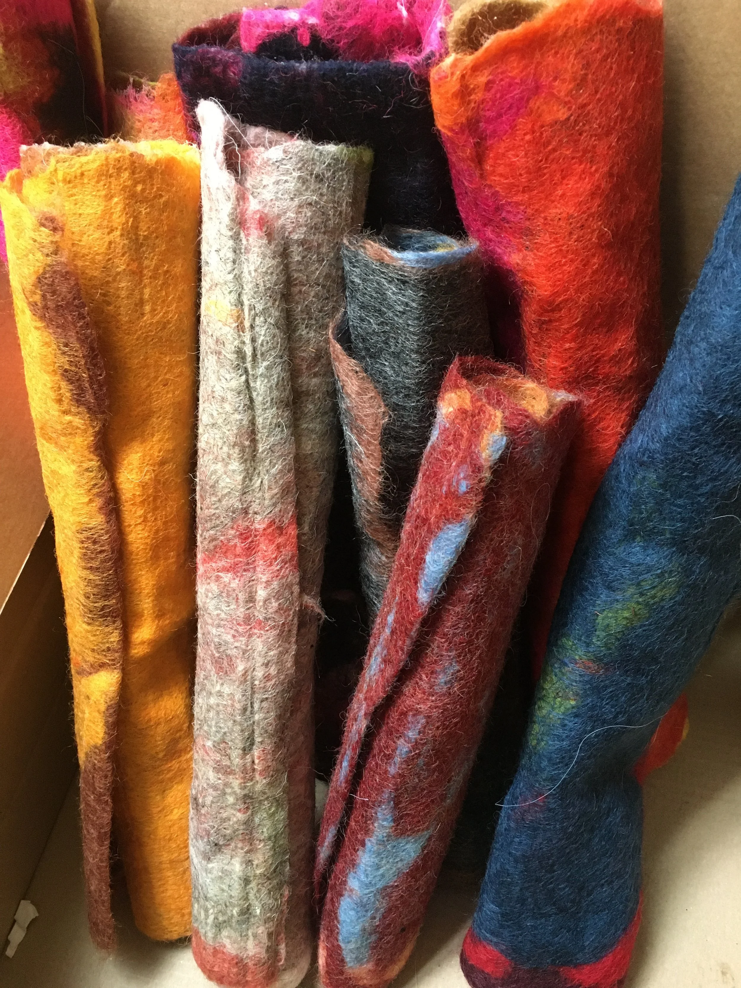 Close-up of colorful felted wool scarves hanging vertically with various patterns and textures.