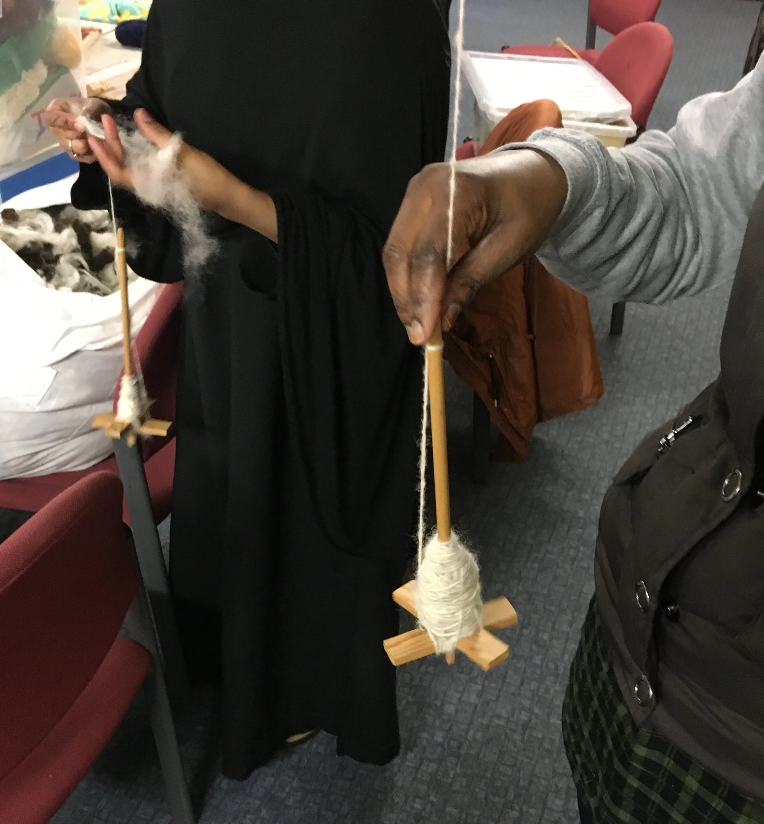 Two people are displaying a small dog with black and white fur on a wooden stand with a spindle of yarn.
