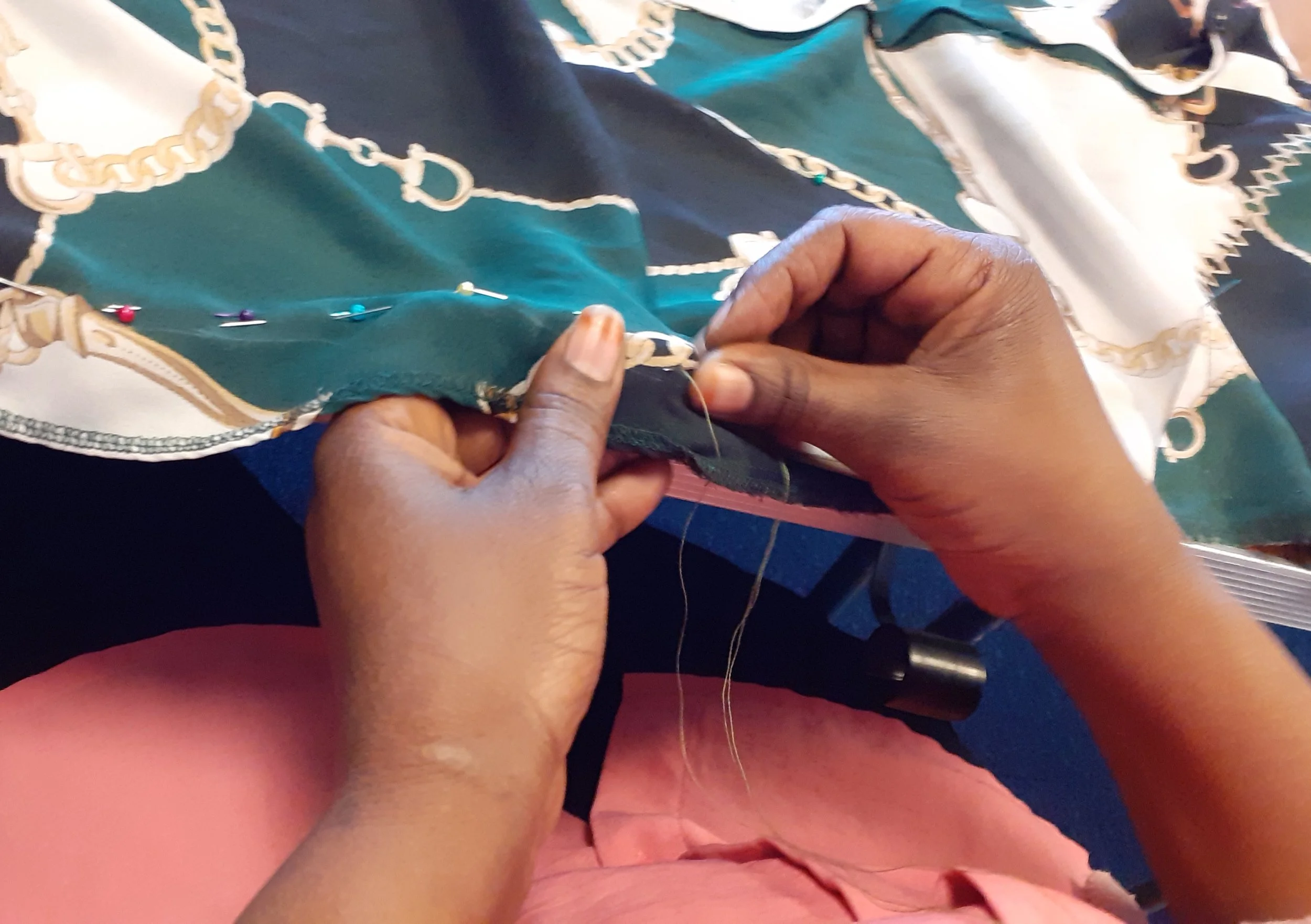 Close-up of hands sewing fabric with a needle and thread, surrounded by colorful push pins on a patterned fabric surface.