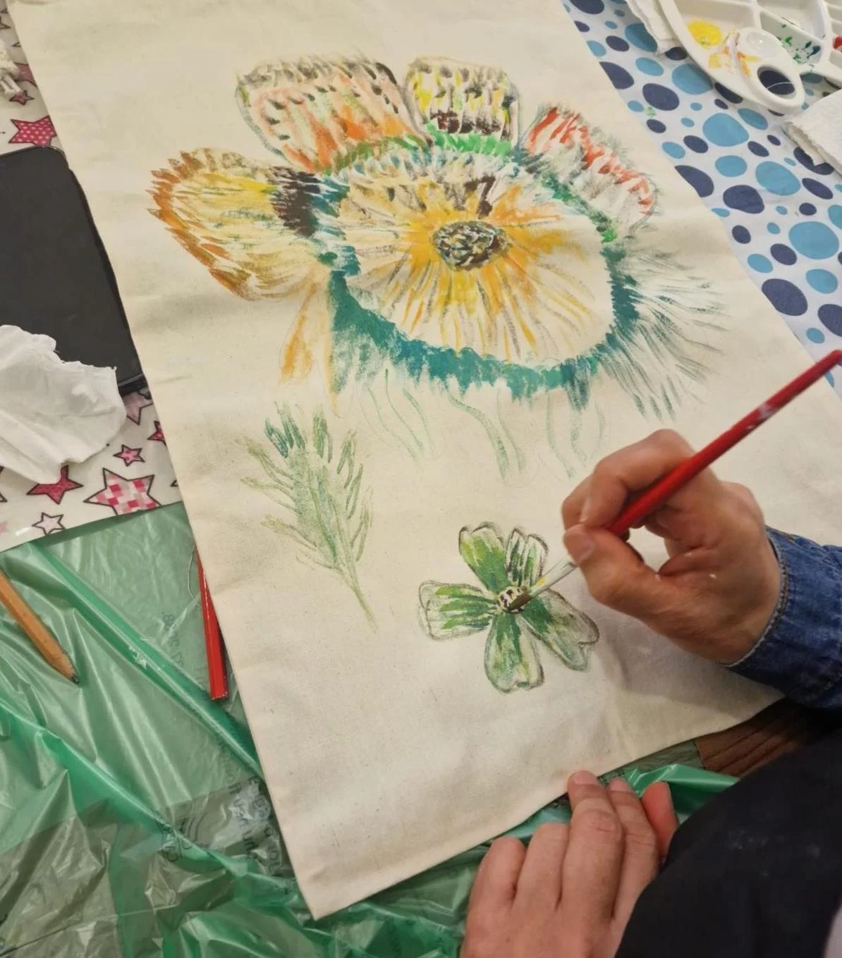 Person painting a colorful flower and butterfly on a large sheet of paper with watercolors and brushes.