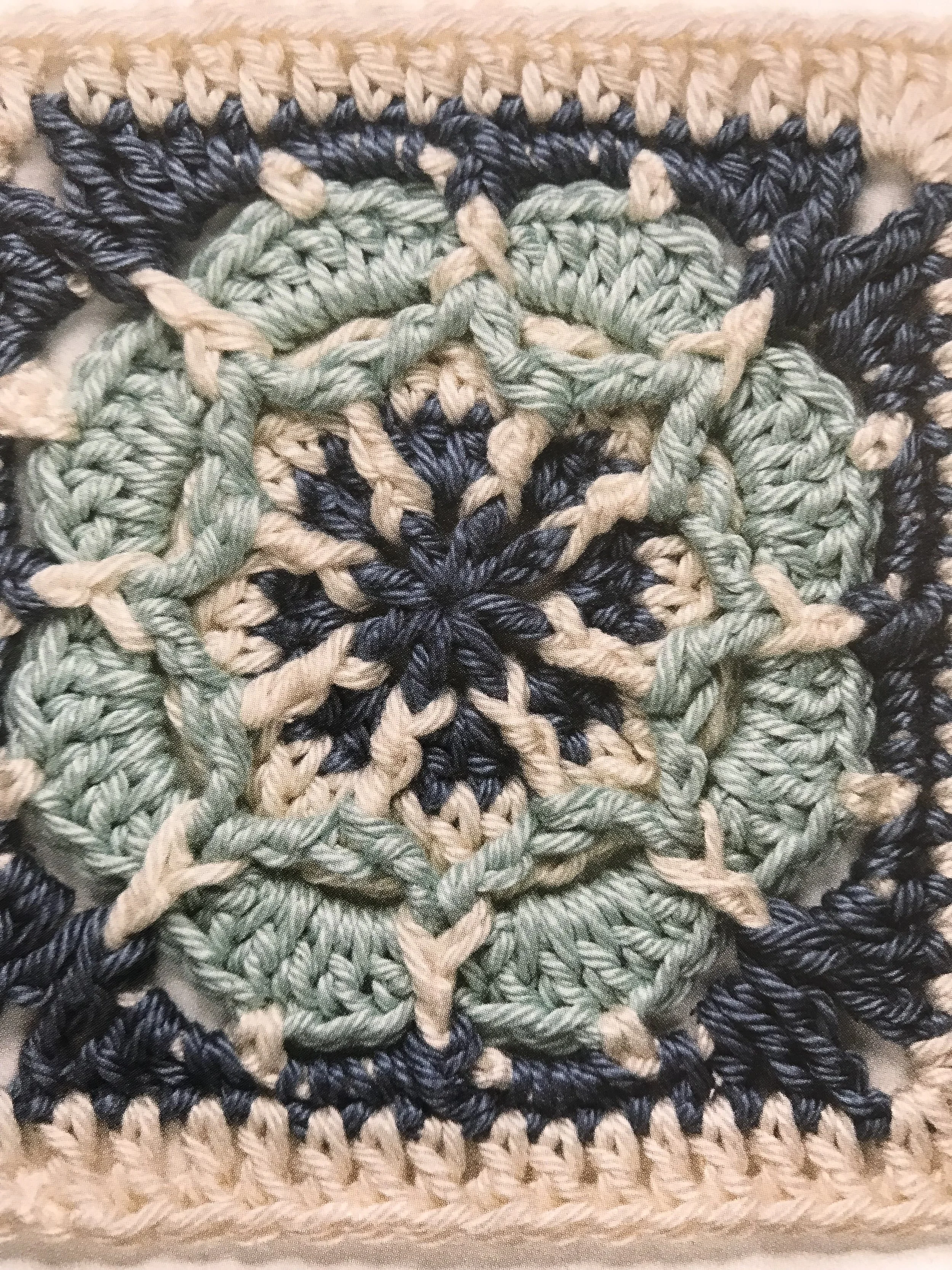 Close-up of a multi-colored woven textile pattern with concentric circular designs in beige, dark blue, and greenish hues.