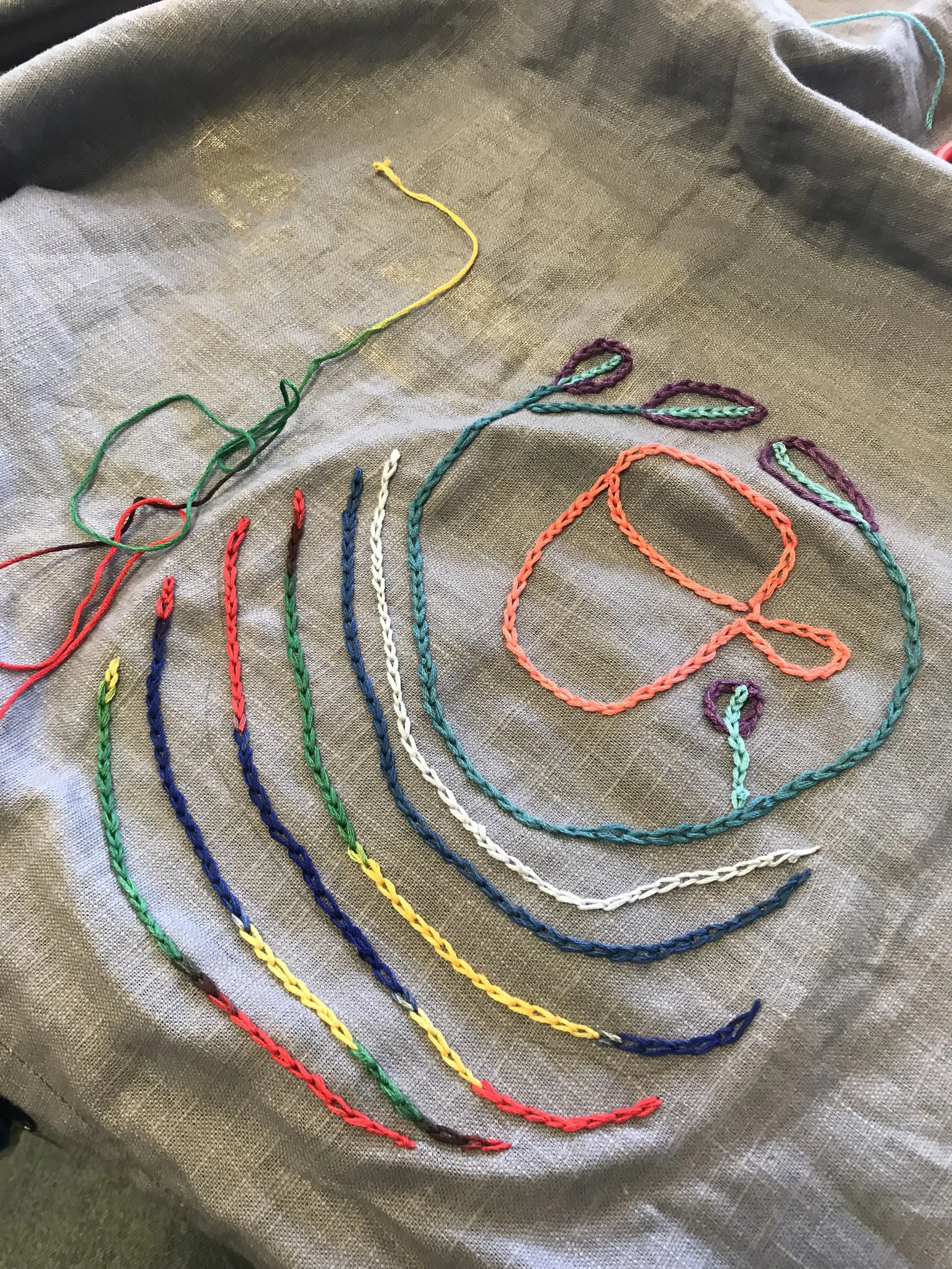 Colorful embroidery floss strings arranged in a pattern on a gray fabric background.
