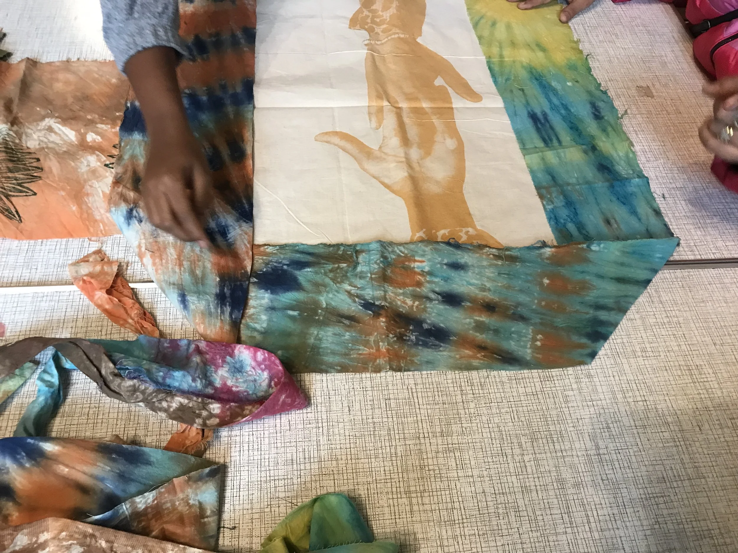 People painting and tie-dyeing fabric with colorful, rainbow and multicolored designs on a table.