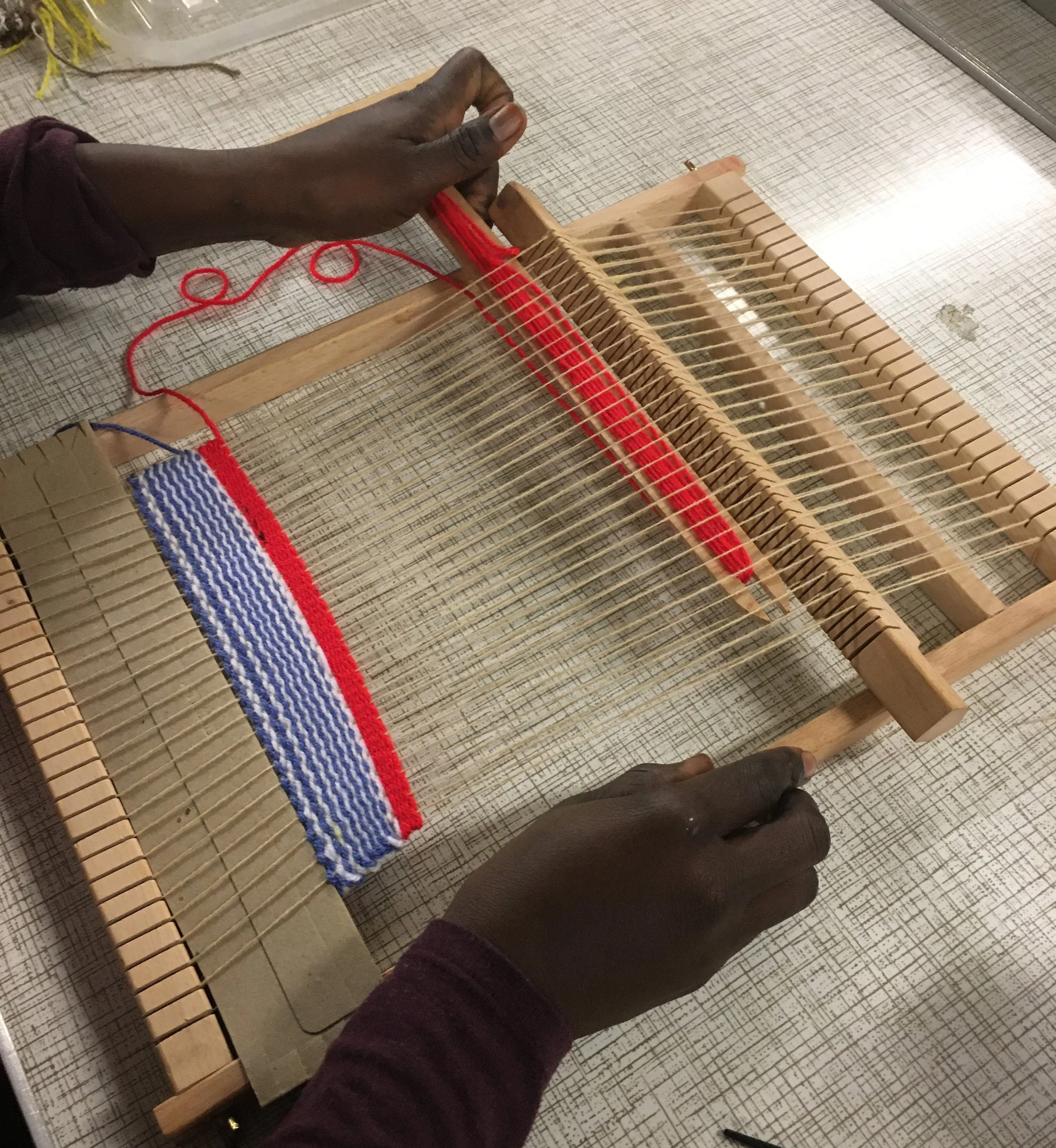 Person using a loom to weave fabric with red, white, and blue colors.