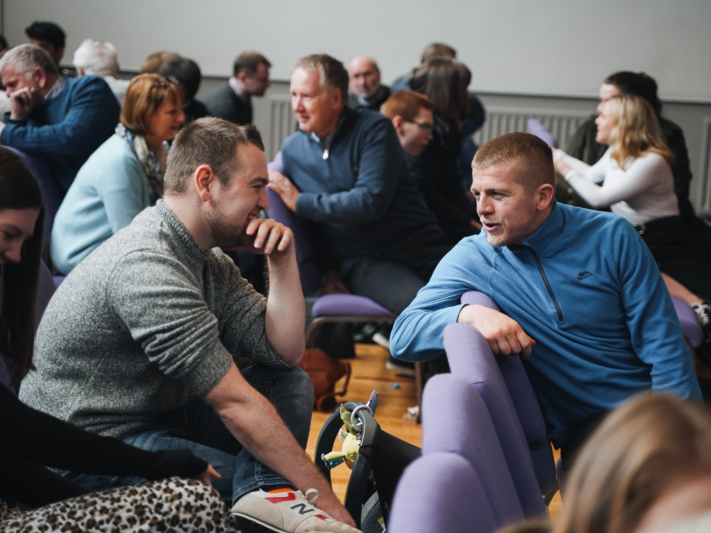 People sitting in chairs and engaging in conversations in a room, likely at a social or networking event.