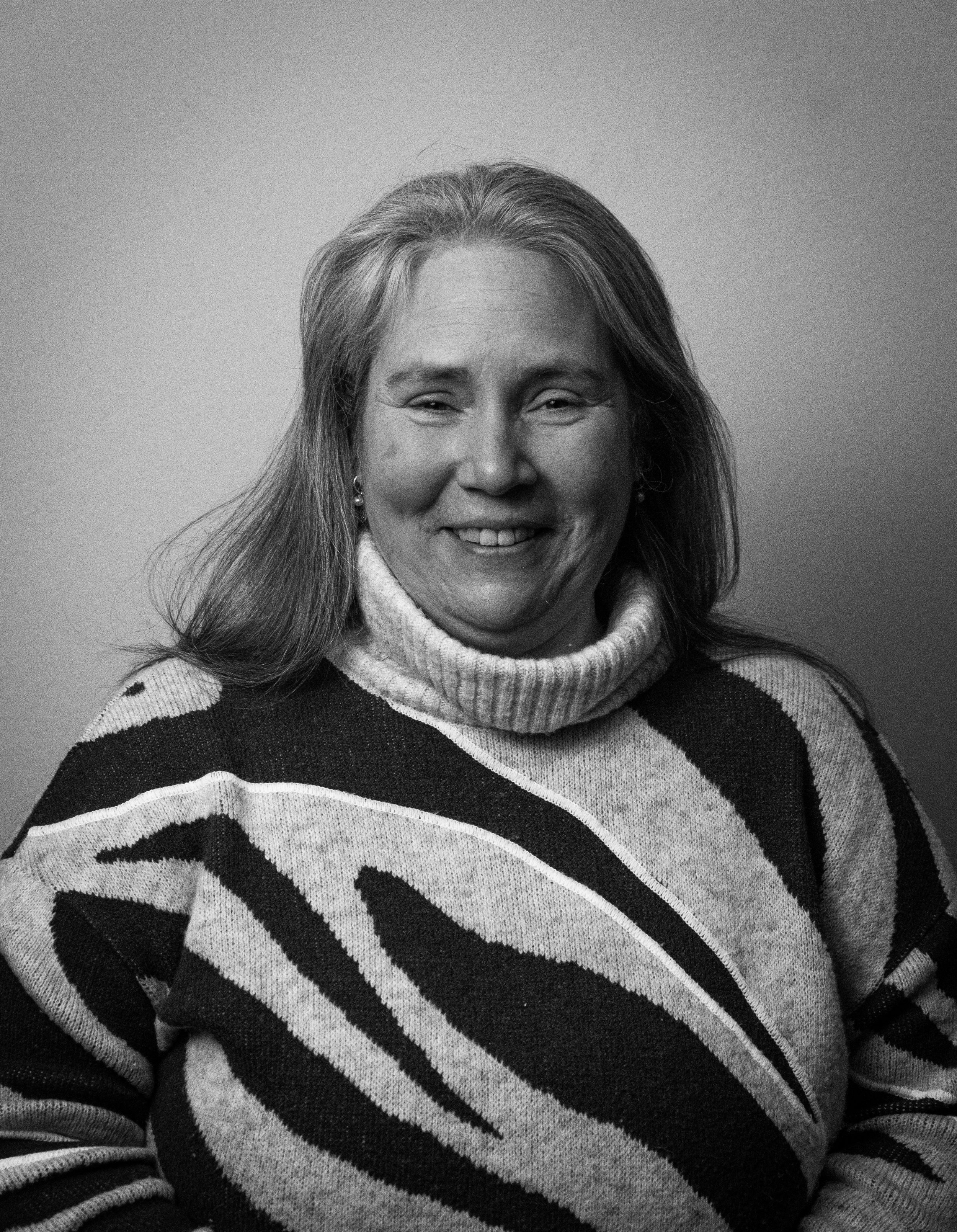 Black and white photo of a smiling woman with long hair, wearing a striped turtleneck sweater.