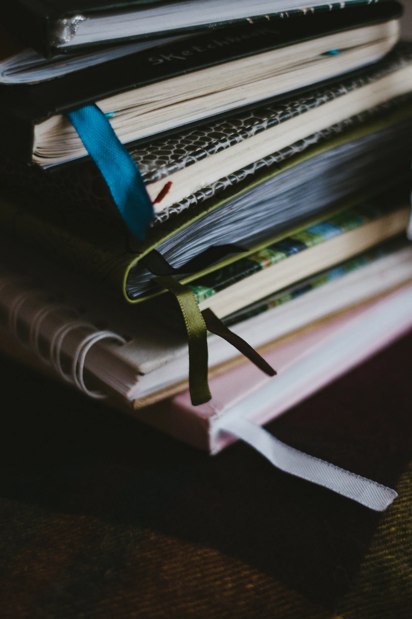 Stacked notebooks and journals with various covers, ribbons, and bookmarks.