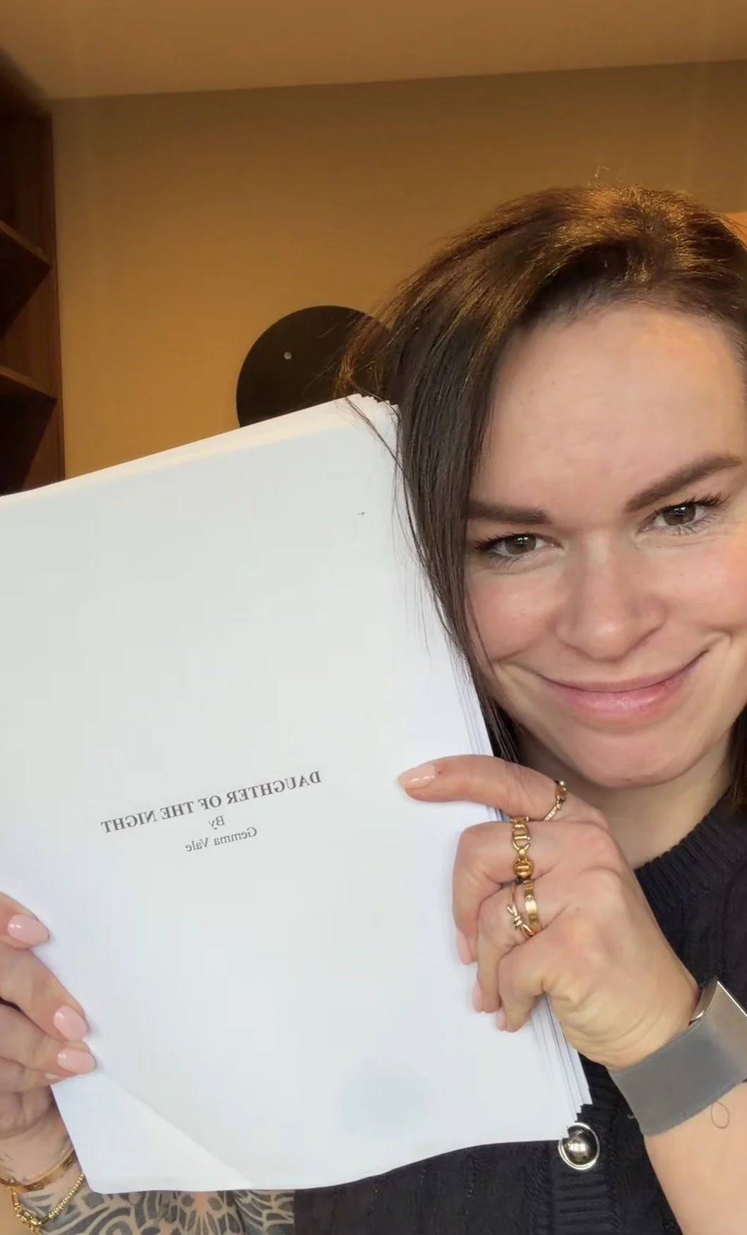 A smiling woman holding a white book titled 'DAUGHTER OF THE NIGHT' by Camila Yule.