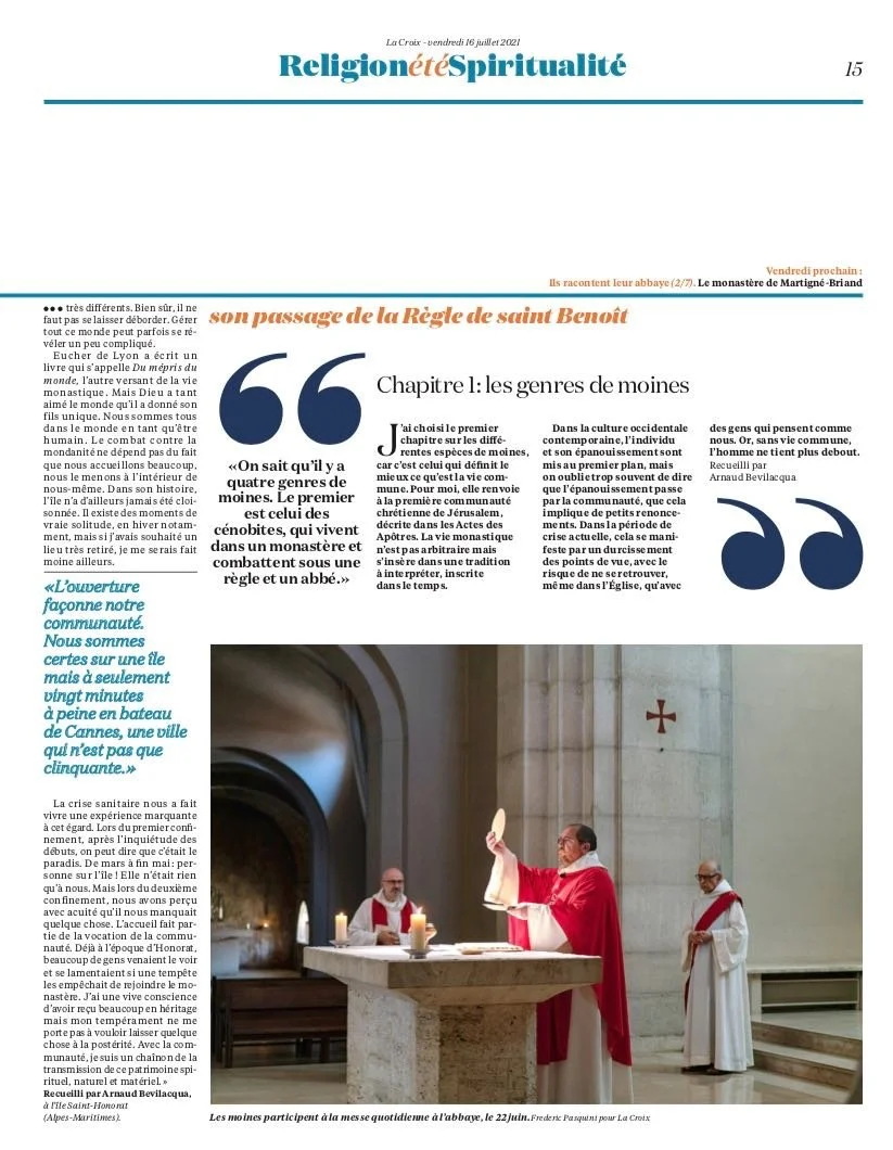 Photograph of monks participating in a daily mass at a church, with one monk holding a bread and the others standing behind an altar with lit candles.