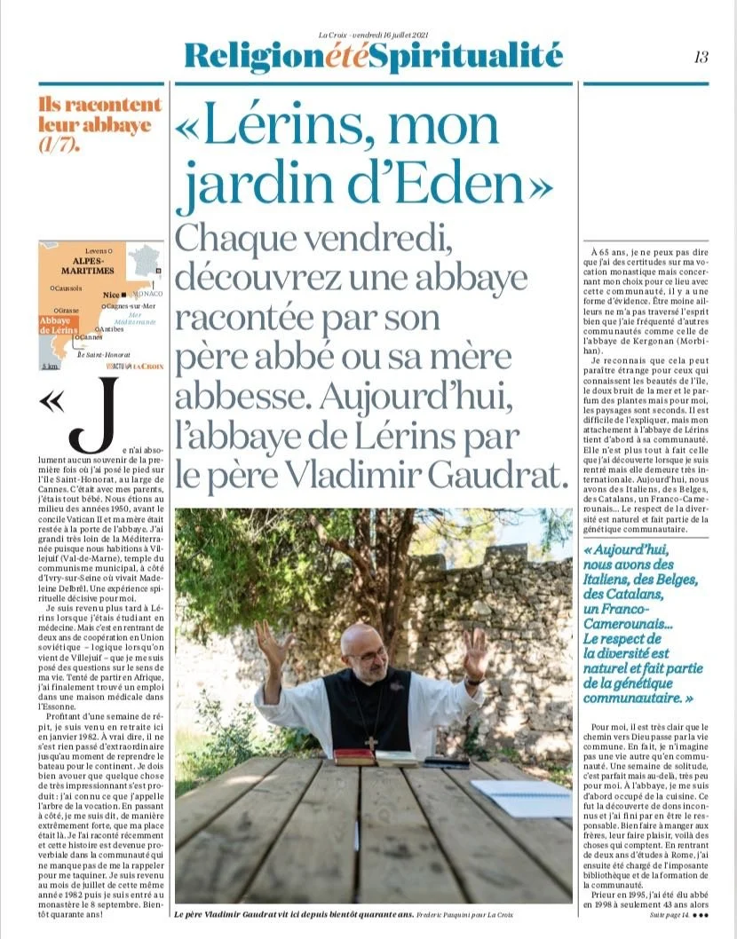 A newspaper article titled 'Lérins, mon jardin d’Eden.' The article features a photograph of an elderly man with a beard wearing a white shirt with a black vest, with his arms raised in front of a natural outdoor setting with trees and blue sky. The 