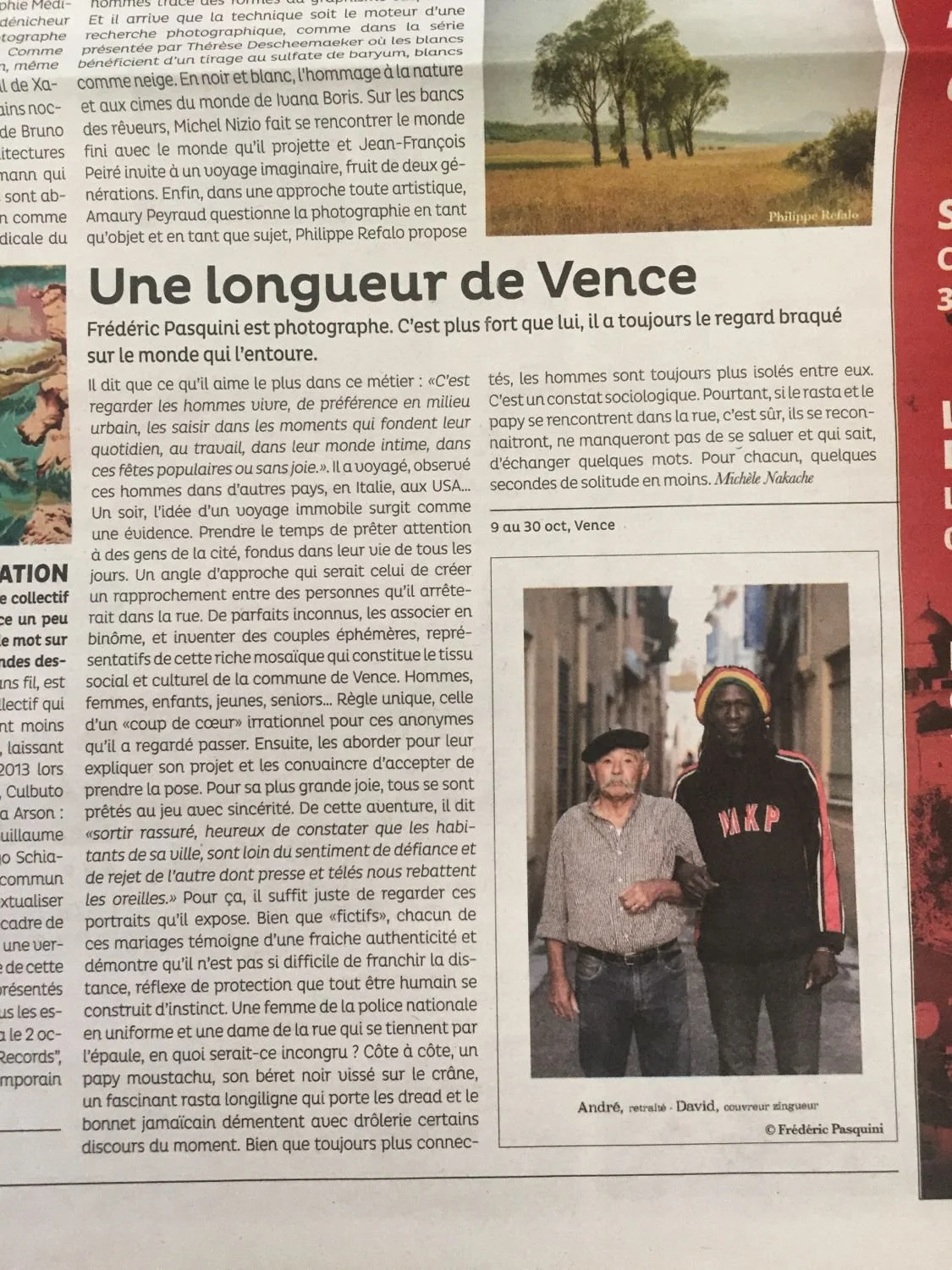 Photograph of two men standing on a street. The man on the left is elderly with a beard, wearing a cap and a patterned shirt. The man on the right is younger, with dark skin, dreadlocks, and a colorful beanie, wearing a black hoodie with red and whit